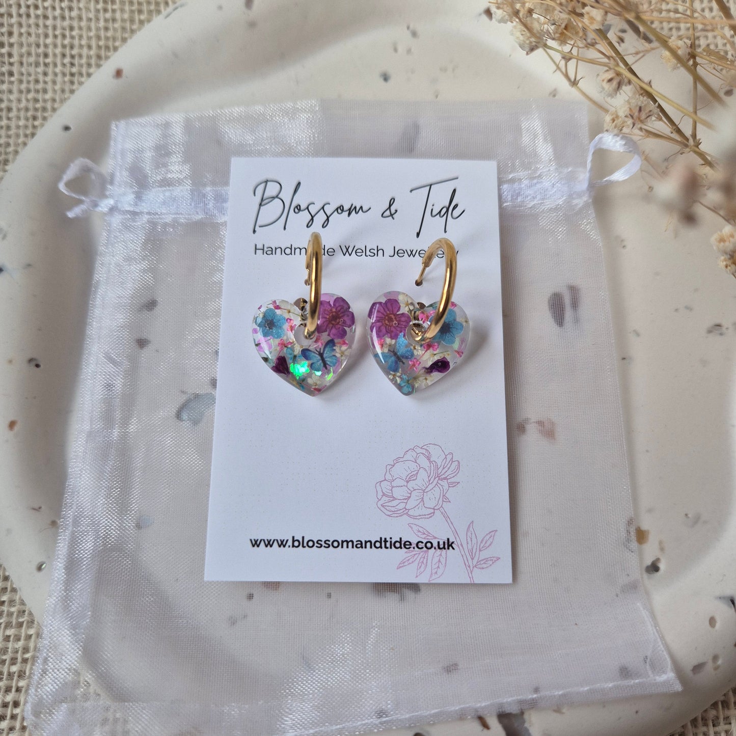Heart shaped earrings with butterflies and flowers on gold hoop. set on a branded card.
