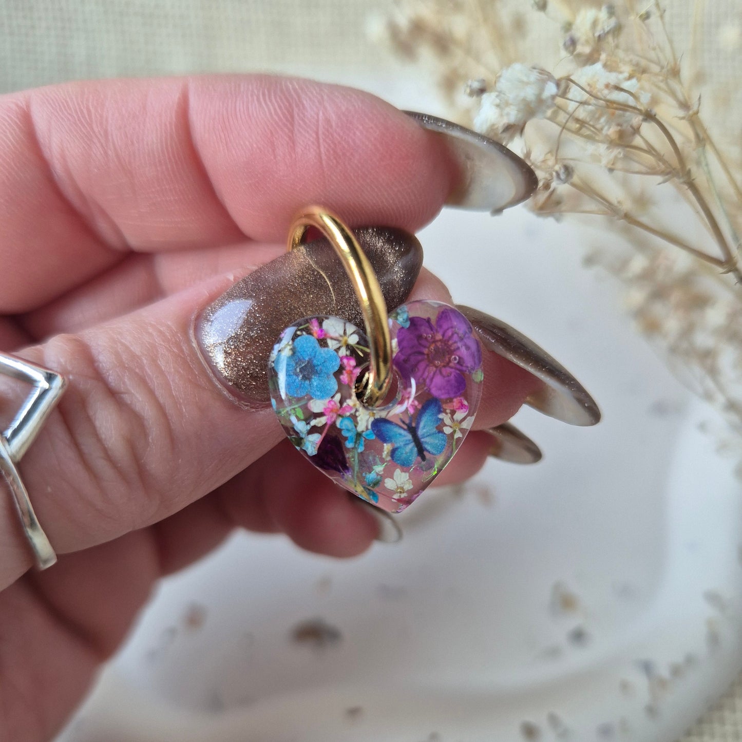 Close up of heart shaped earring on a gold hoop. With blue butterflies and purple flowers.