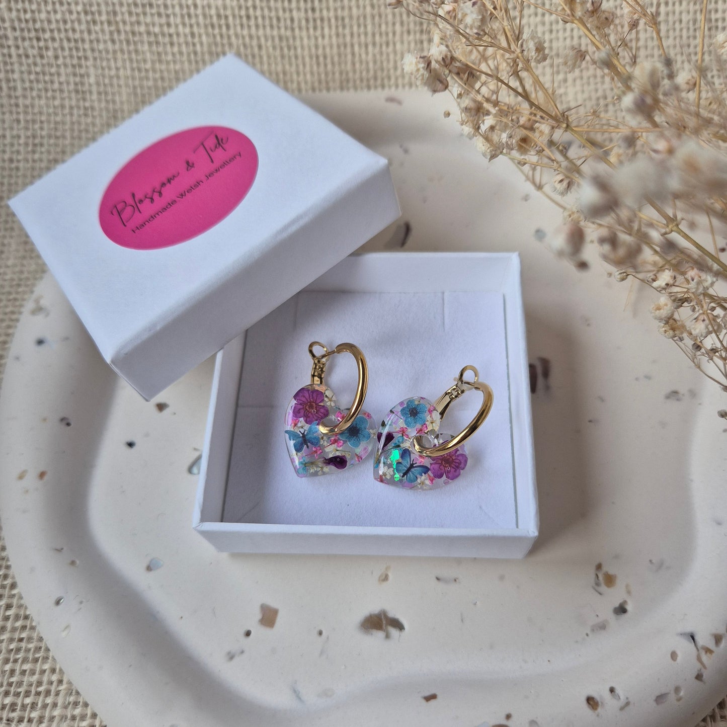 Colorful earrings in a box on a textured surface with a pink card.