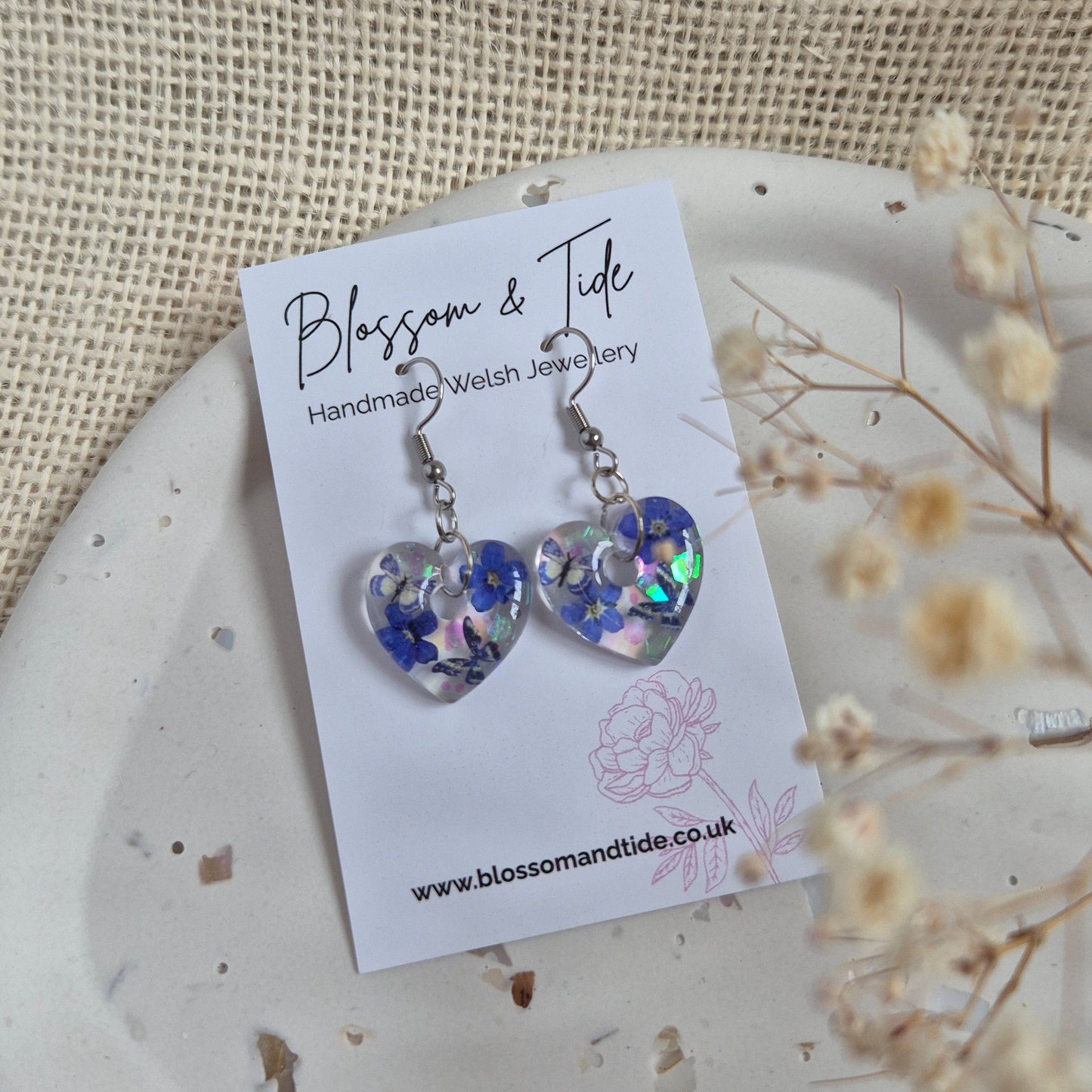 Heart shaped earrings with real pressed forget-me-nots and blue butterflies on stainless steel hook. Presented on a branded Blossom & Tide card.