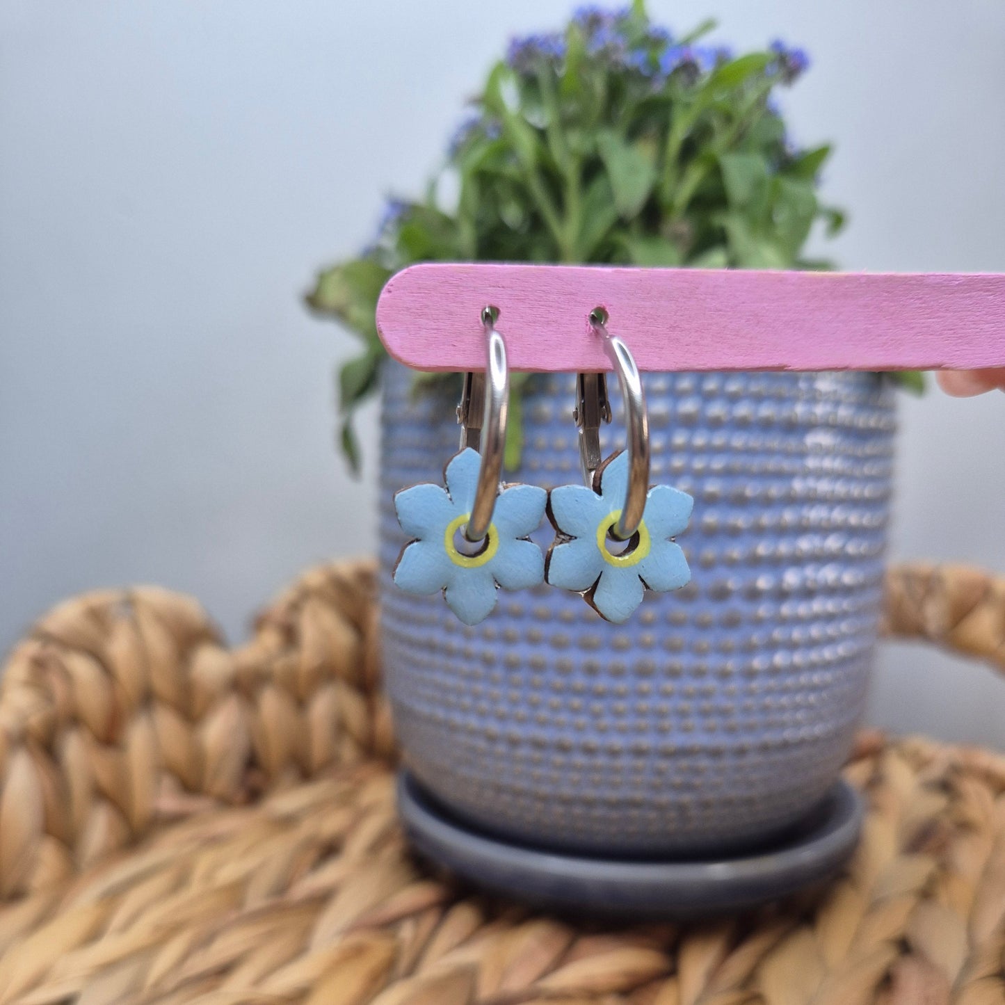 A pair of hand-painted hoop earrings featuring intricate forget-me-not flowers, sealed with a glossy resin topcoat, displayed on stainless steel hoops. Also available in a matte finish.