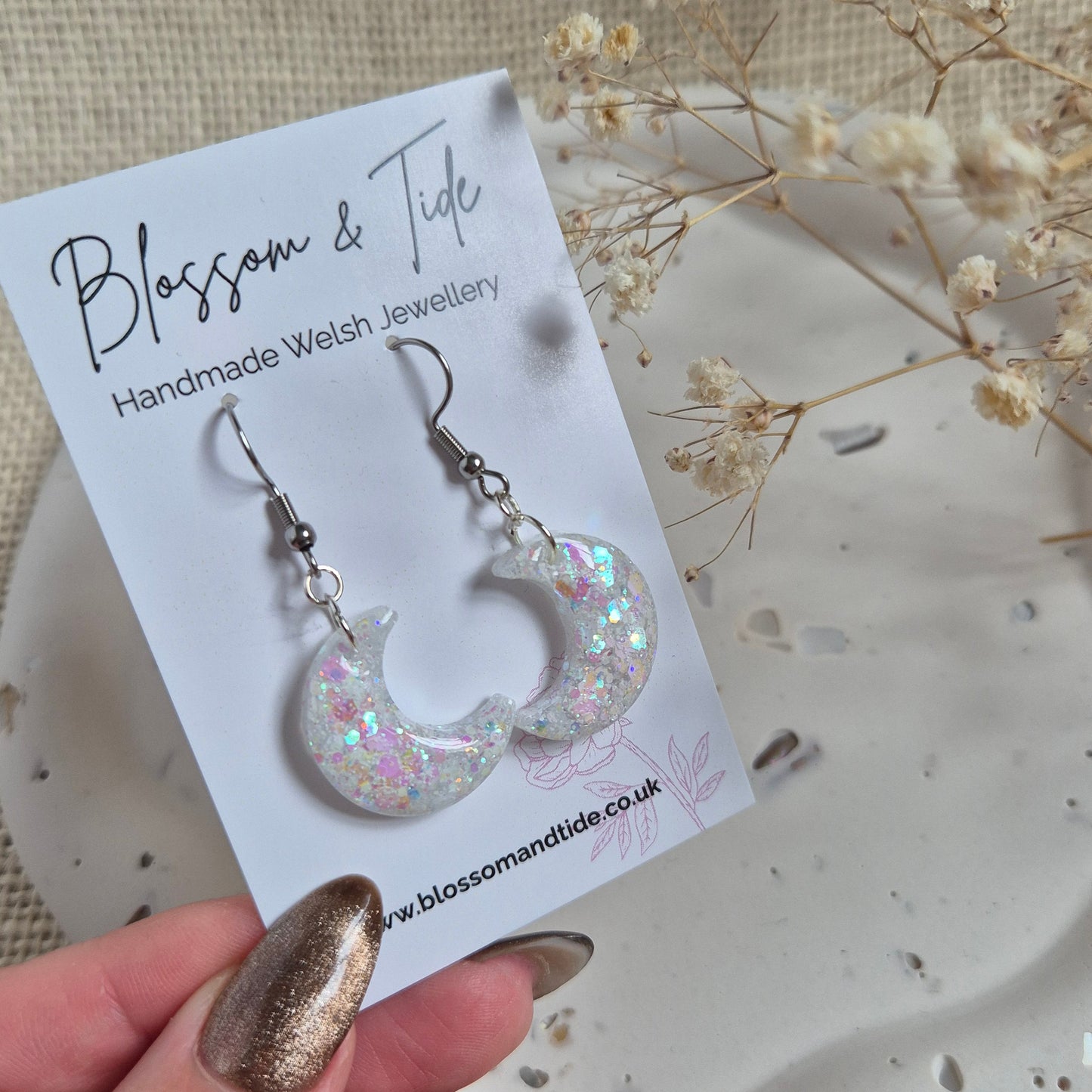 Close-up of handmade half moon earrings catching light in pink and blue tones.