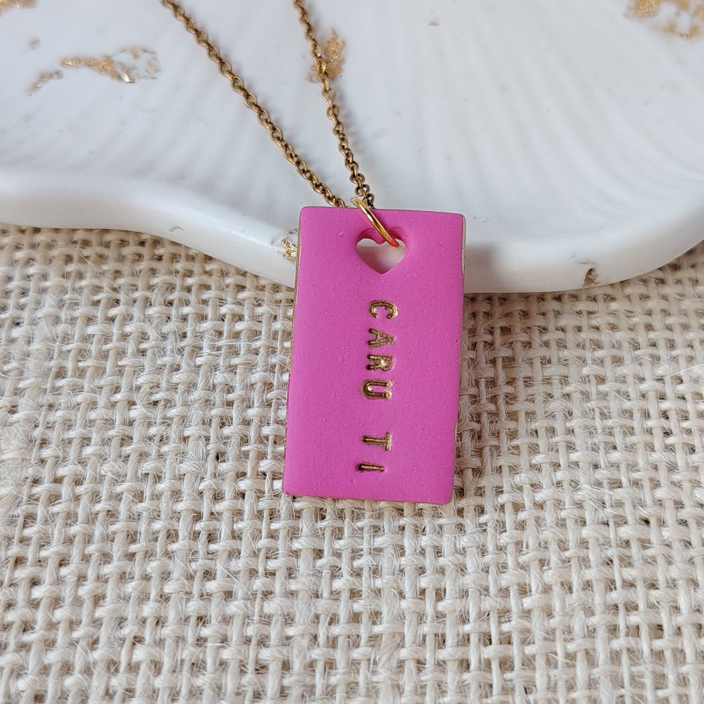 Pink polymer clay rectangle necklace with gold hand-painted accents, heart cut-out and the Welsh words Caru Ti on a gold stainless steel chain.