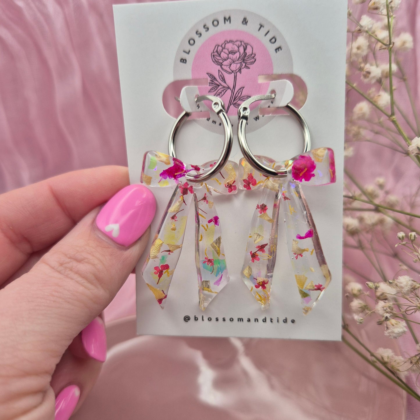 Handmade resin bow hoop earrings with real pink and yellow flower petals and shimmering mylar flakes.