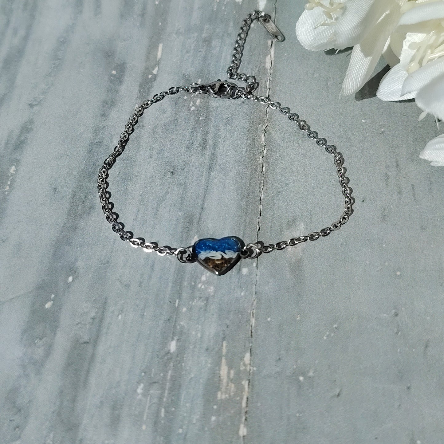 Bracelet with a blue heart charm on a wooden surface with white flowers.