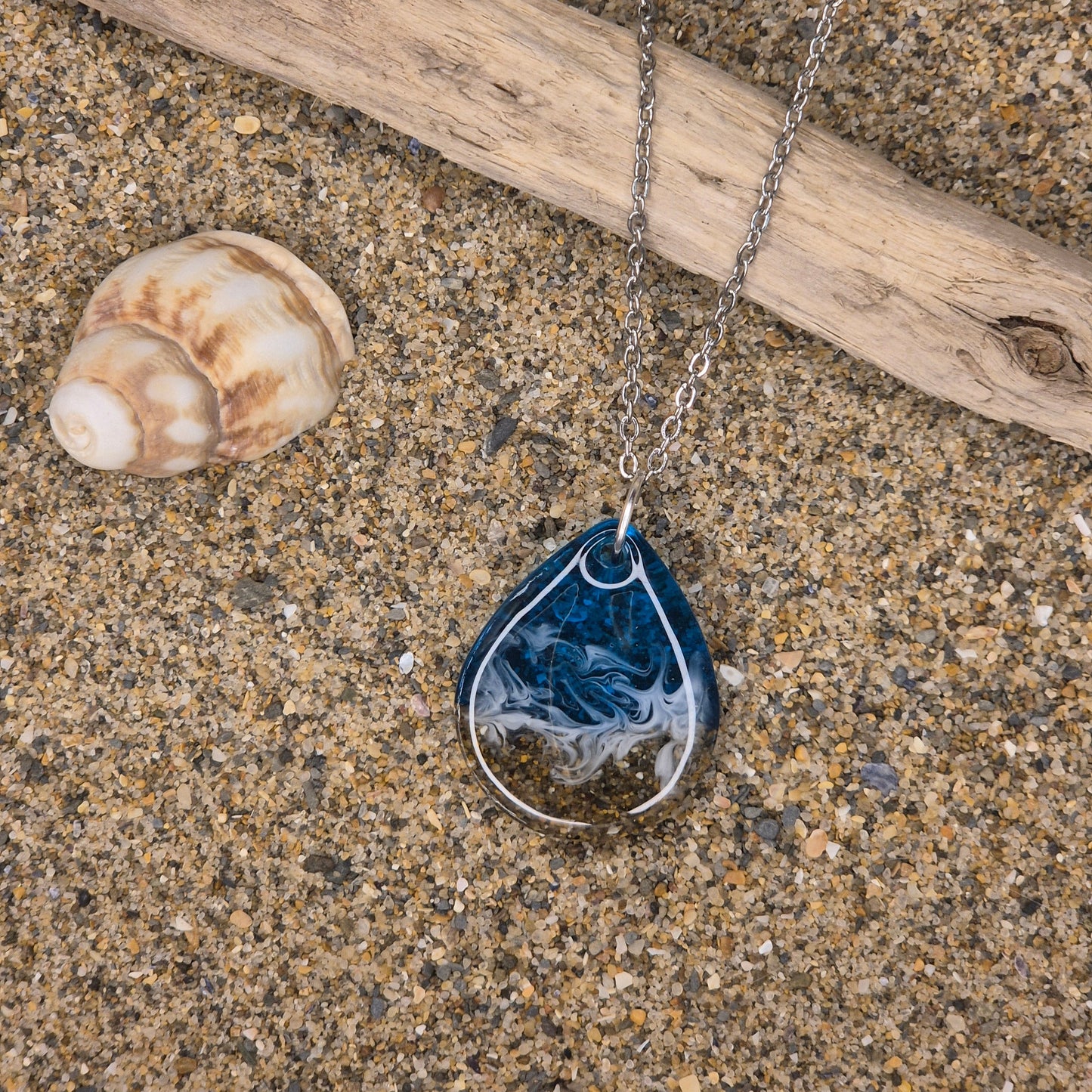 Handmade blue teardrop necklace. Made with real sand from Welsh beaches. Replicating the look of sea and sand. Displayed on a blossom and tide branded card.
