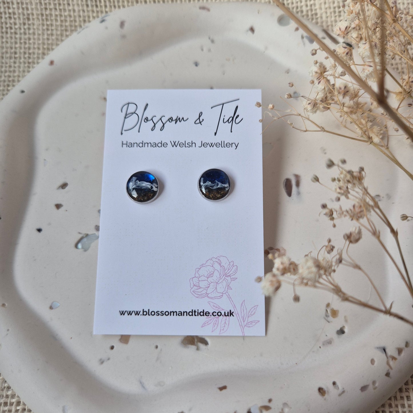 Pair of beach earrings on a branded card with a decorative plate and dried flowers.