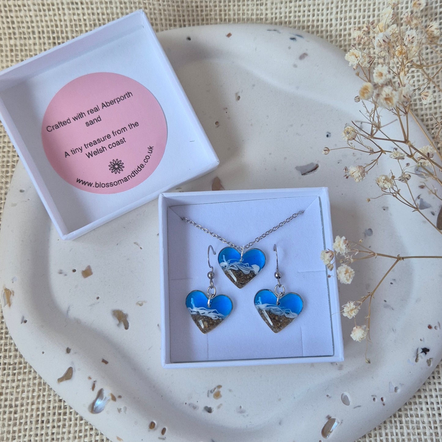 Earring and necklace set with blue heart in a white box on a textured surface