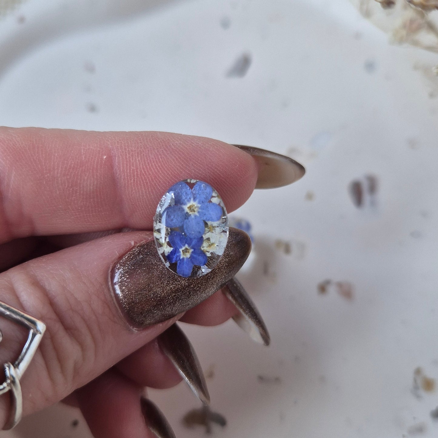 Hand holding a oval earring with a floral design against a blurred background