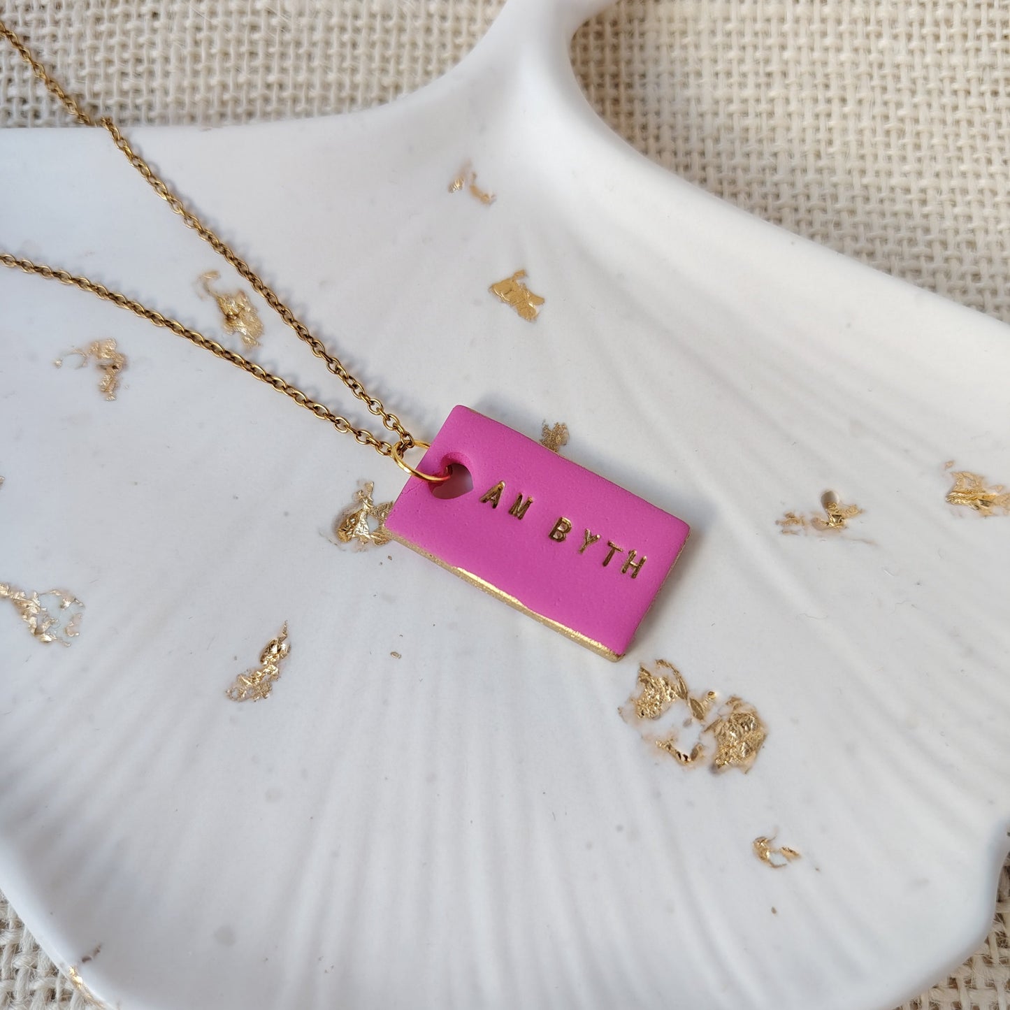 Pink polymer clay rectangle necklace with gold hand-painted accents, heart cut-out and the Welsh words Am Byth on a gold stainless steel chain.