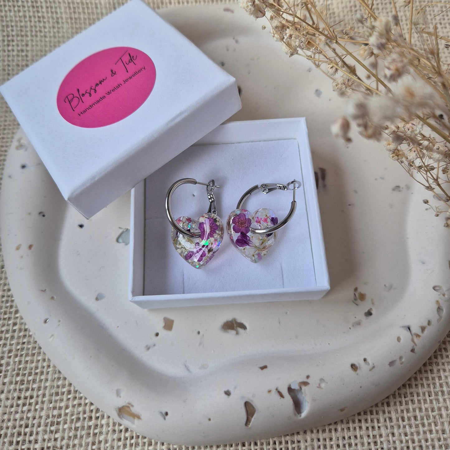 Floral earrings in a box on a textured surface with dried flowers.