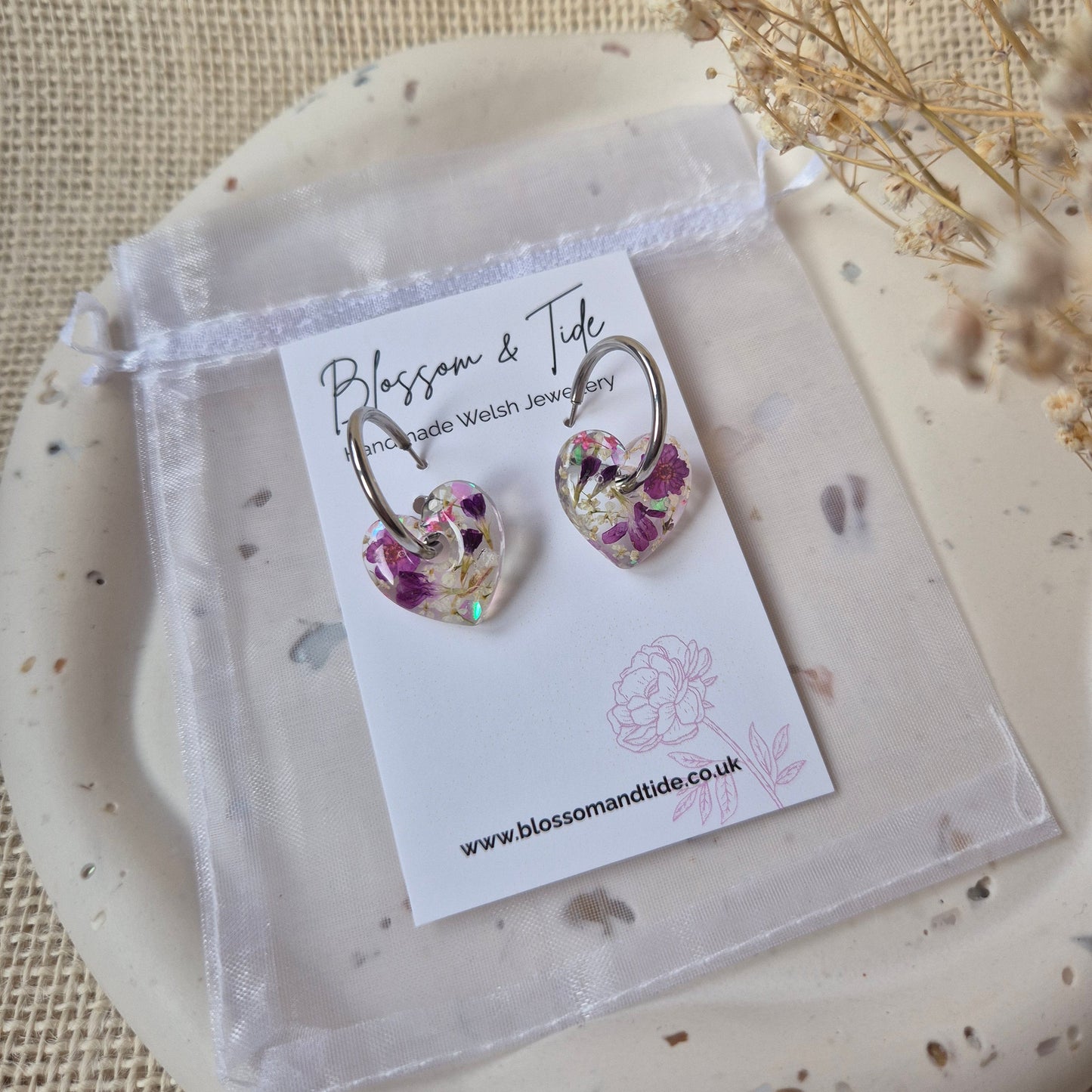 Pair of floral earrings on a branded card with a natural background