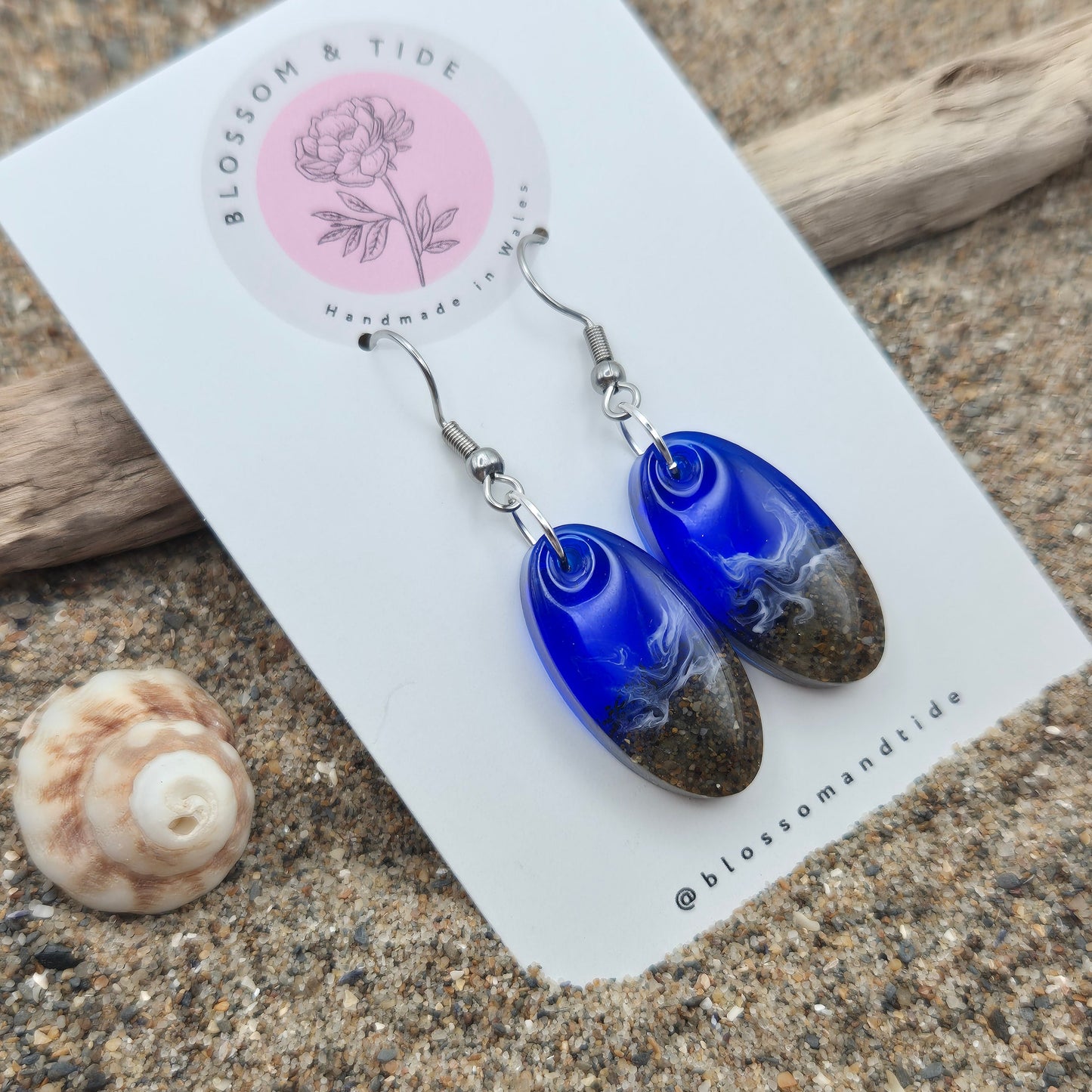 Handmade blue oval drop earrings. Made with real sand from Welsh beaches. Replicating the look of sea and sand. Displayed on a blossom and tide branded earring card.