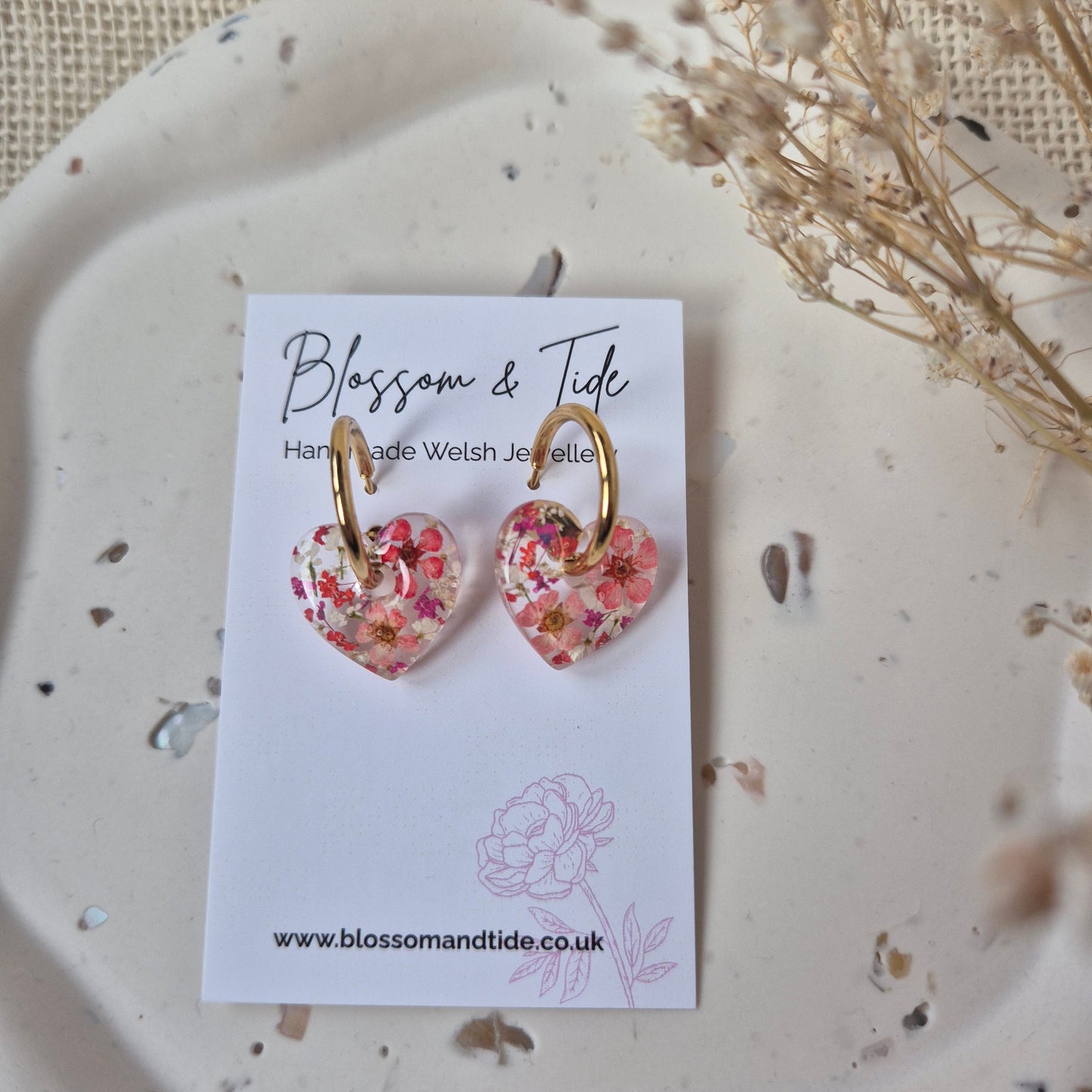 Red and purple heart earrings on gold hoops. On a branded jewellery card