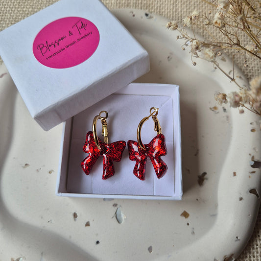 red glitter bow earrings on a gold hoop in a blossom and tide box, against a neutral background