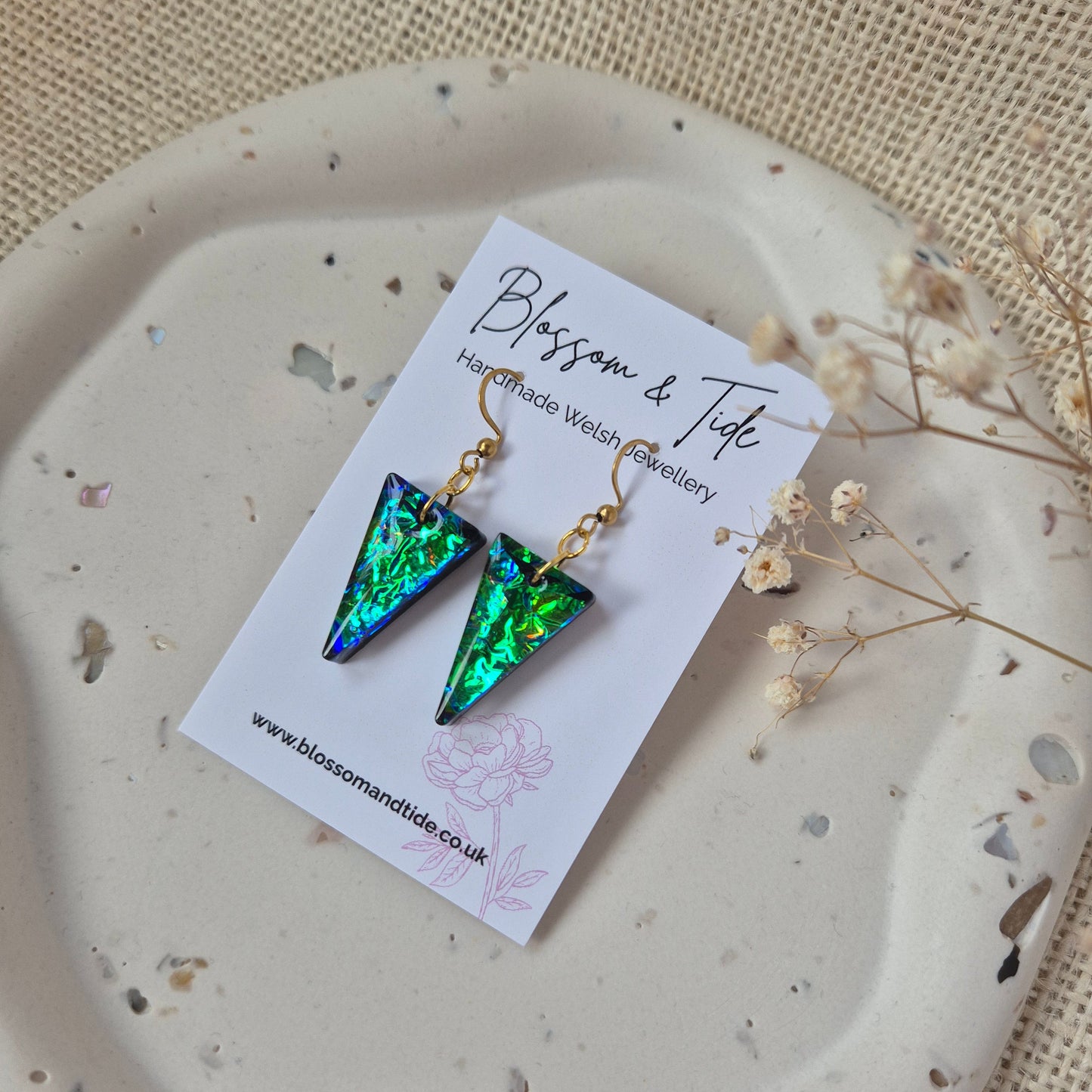 Triangular earrings on a white card with 'Blossom & Tide' branding, displayed on a textured beige surface.