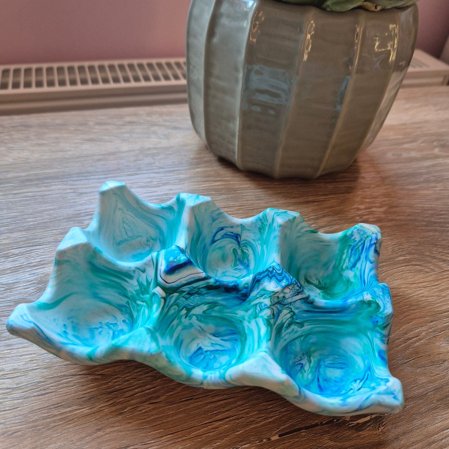 Marble Jesmonite egg holder on a wooden surface with a potted plant in the background.