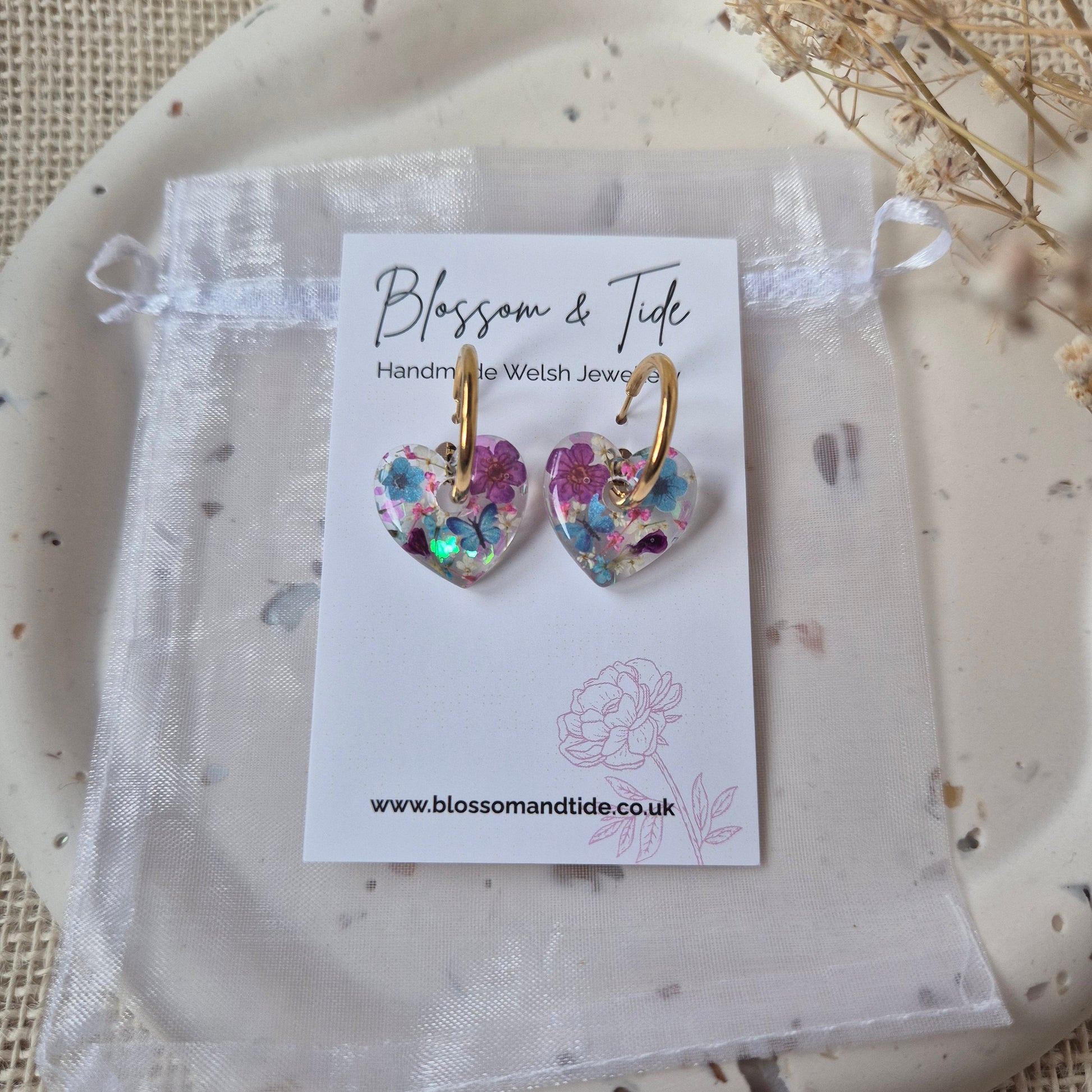 Heart shaped earrings with butterflies and flowers on gold hoop. set on a branded card.