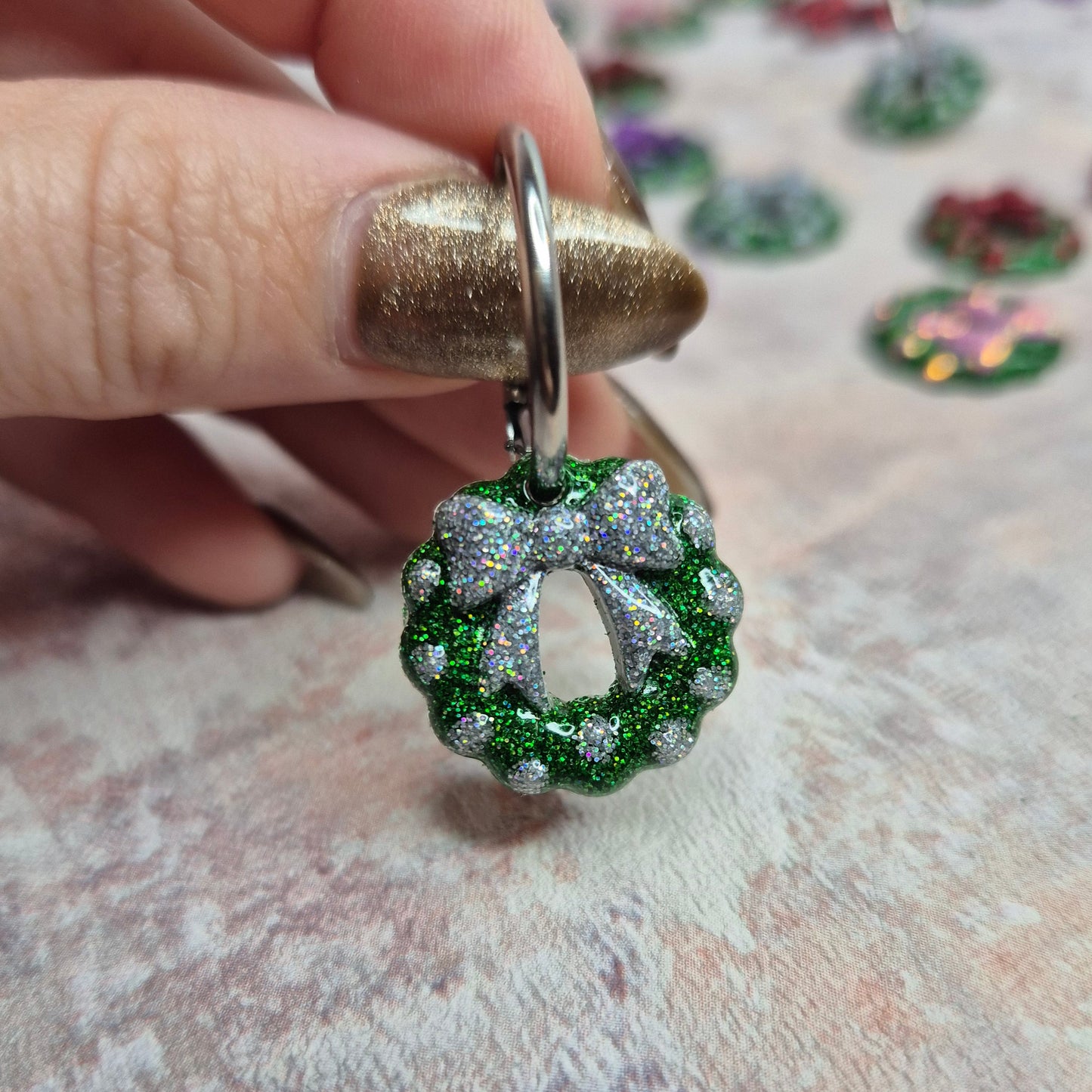 Christmas earrings with green and silver design held by a hand on a textured surface.