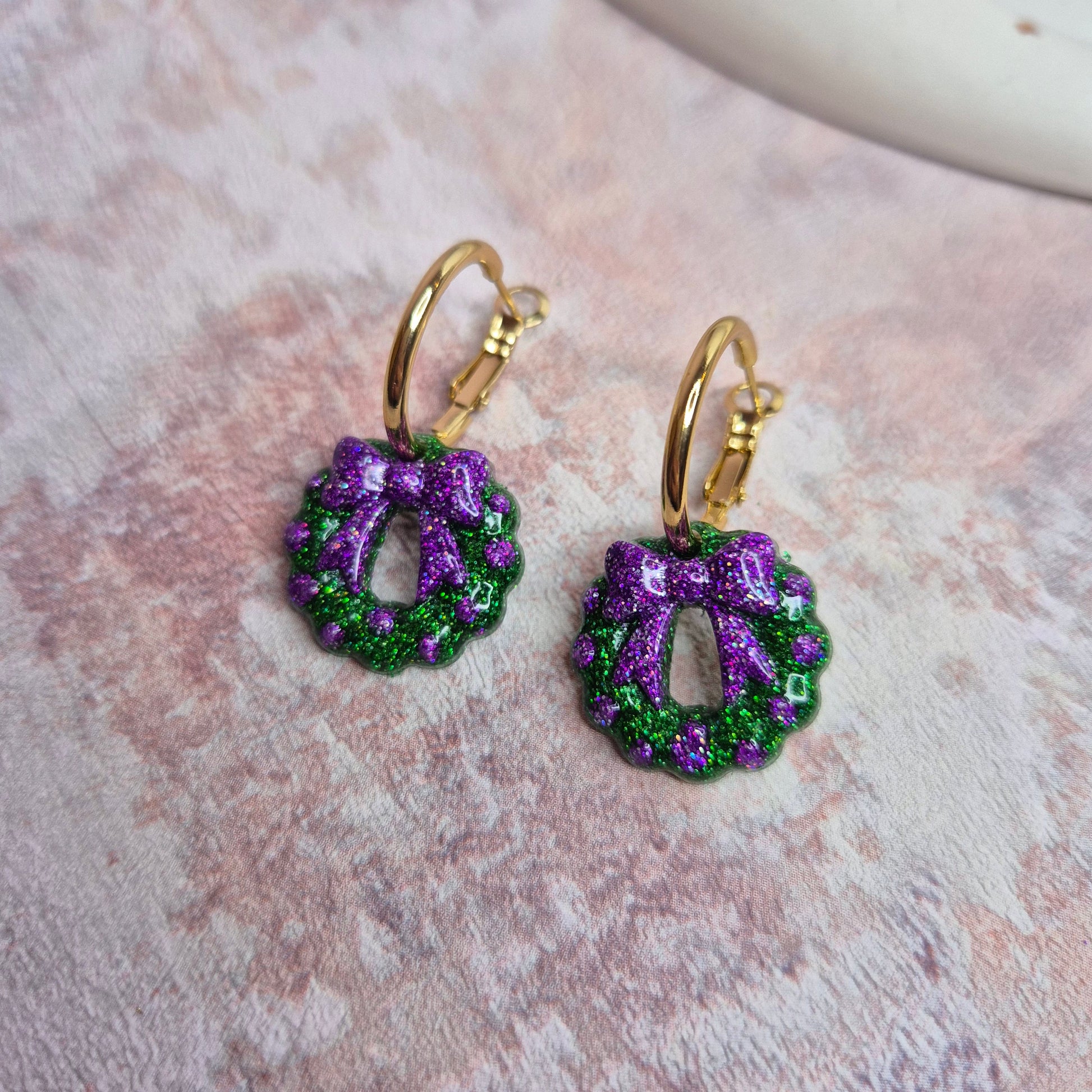 Pair of purple and green glitter hoop earrings on a textured surface