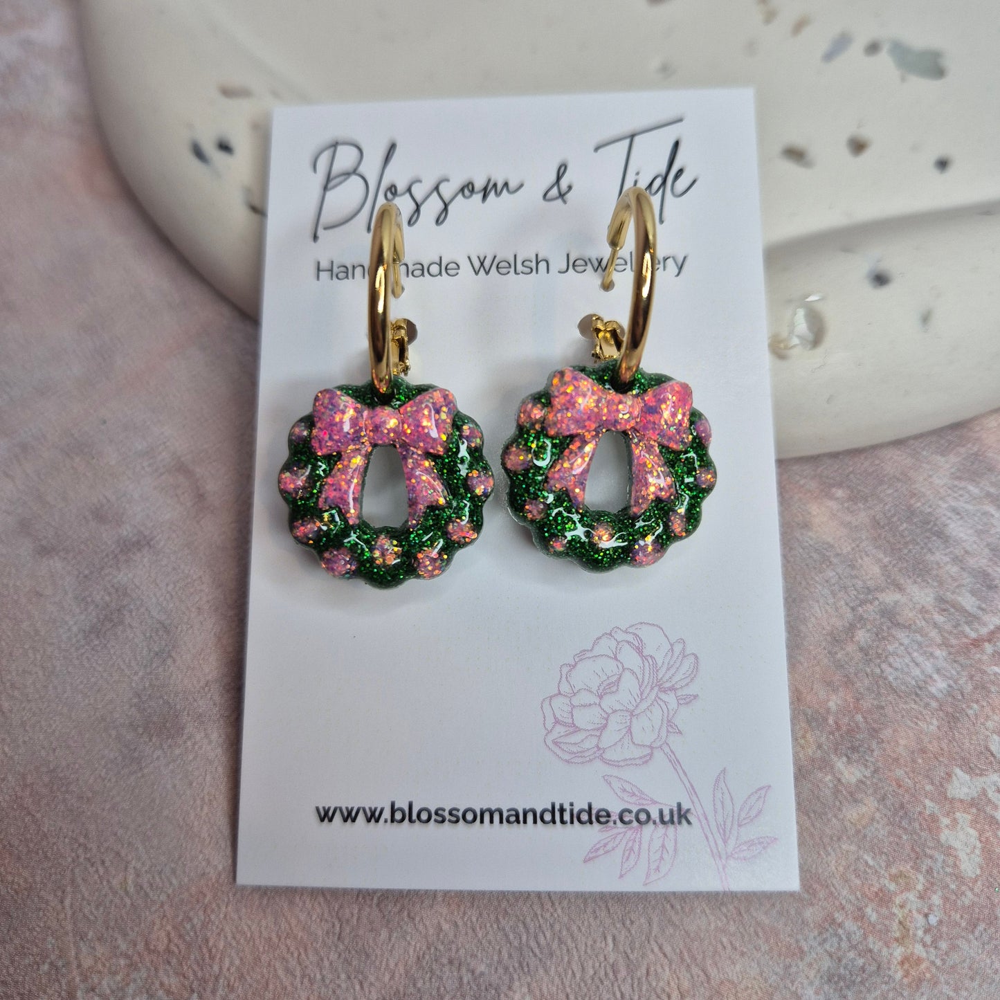 Christmas wreath with pink bow earrings. Glitter earrings displayed on a branded card against a pink background