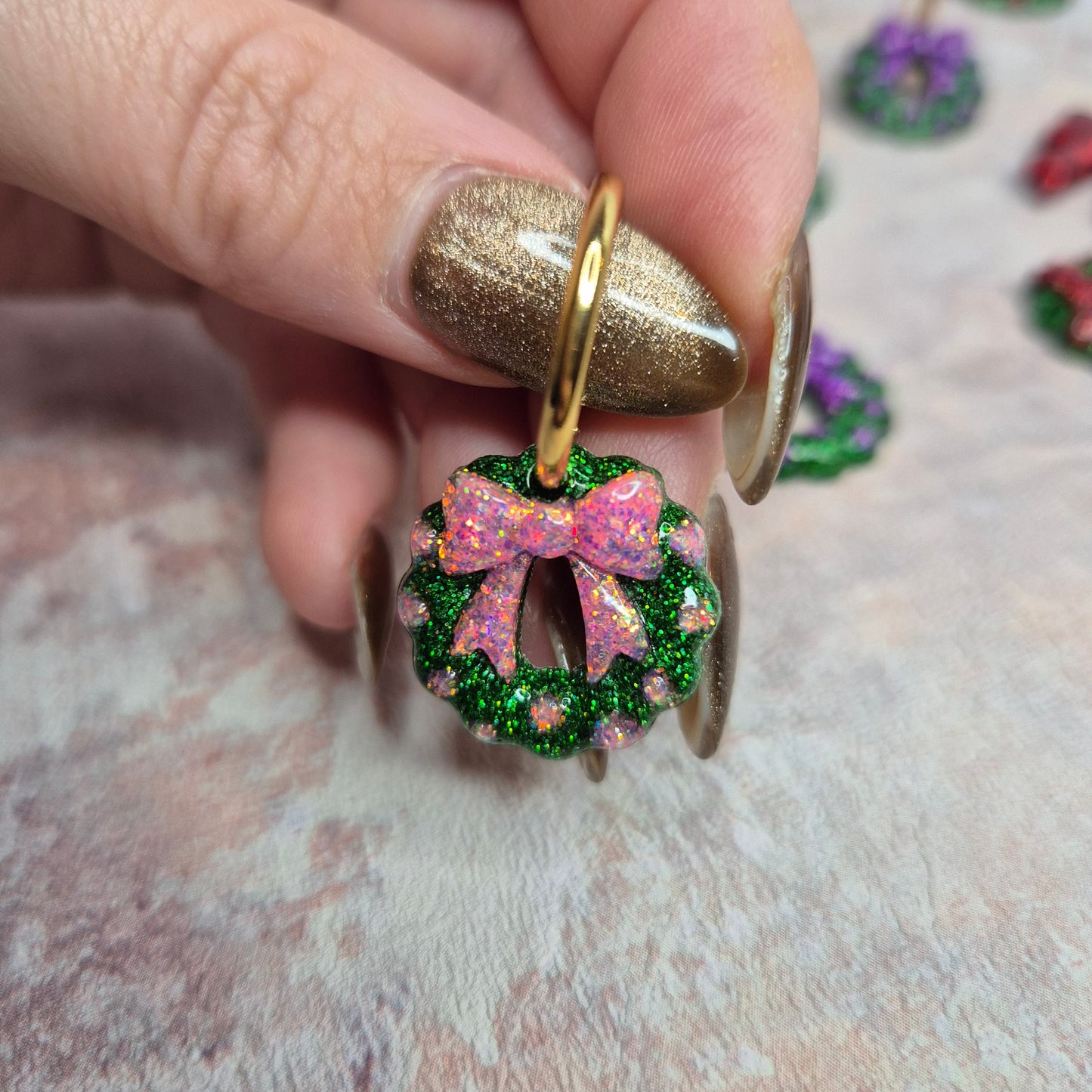 Christmas wreath with pink bow earrings. Glitter earrings being held against a pink background