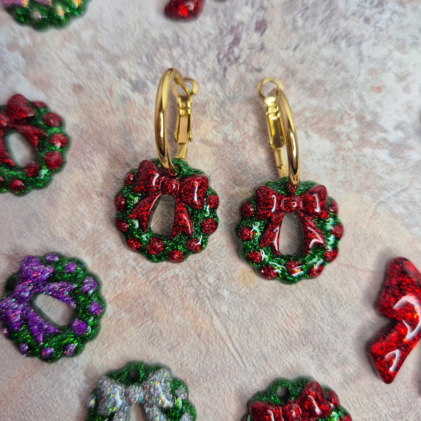 Christmas-themed earrings with wreath and bow designs on a textured surface.