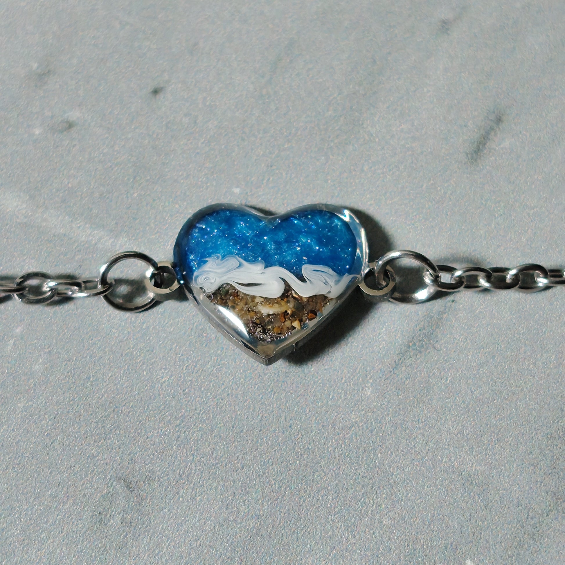 Close up photo of the hand made sand and sea charm on a stainless steel bracelet, against wood background 
