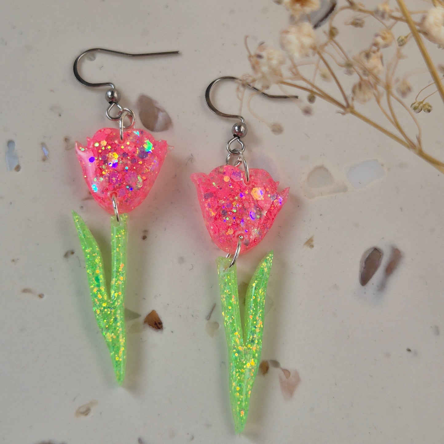 Close-up of glitter tulip earrings showing pink petals and green stem.