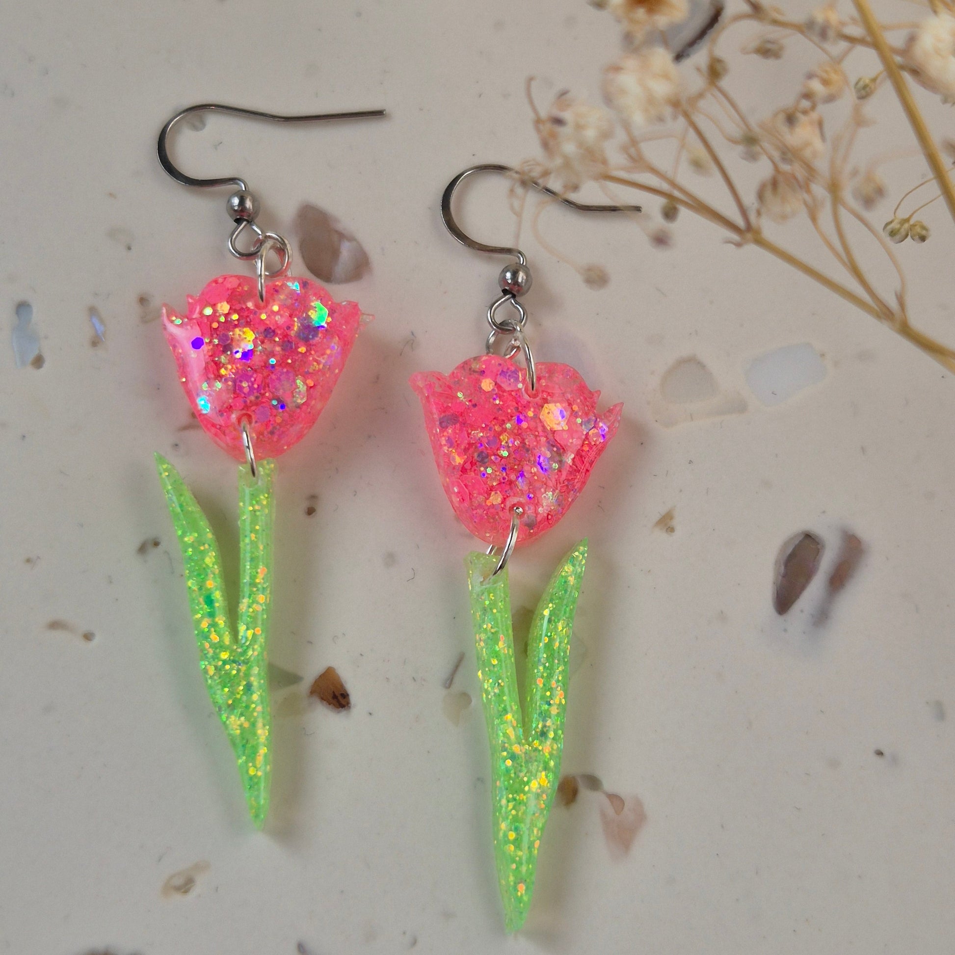 Close-up of glitter tulip earrings showing pink petals and green stem.