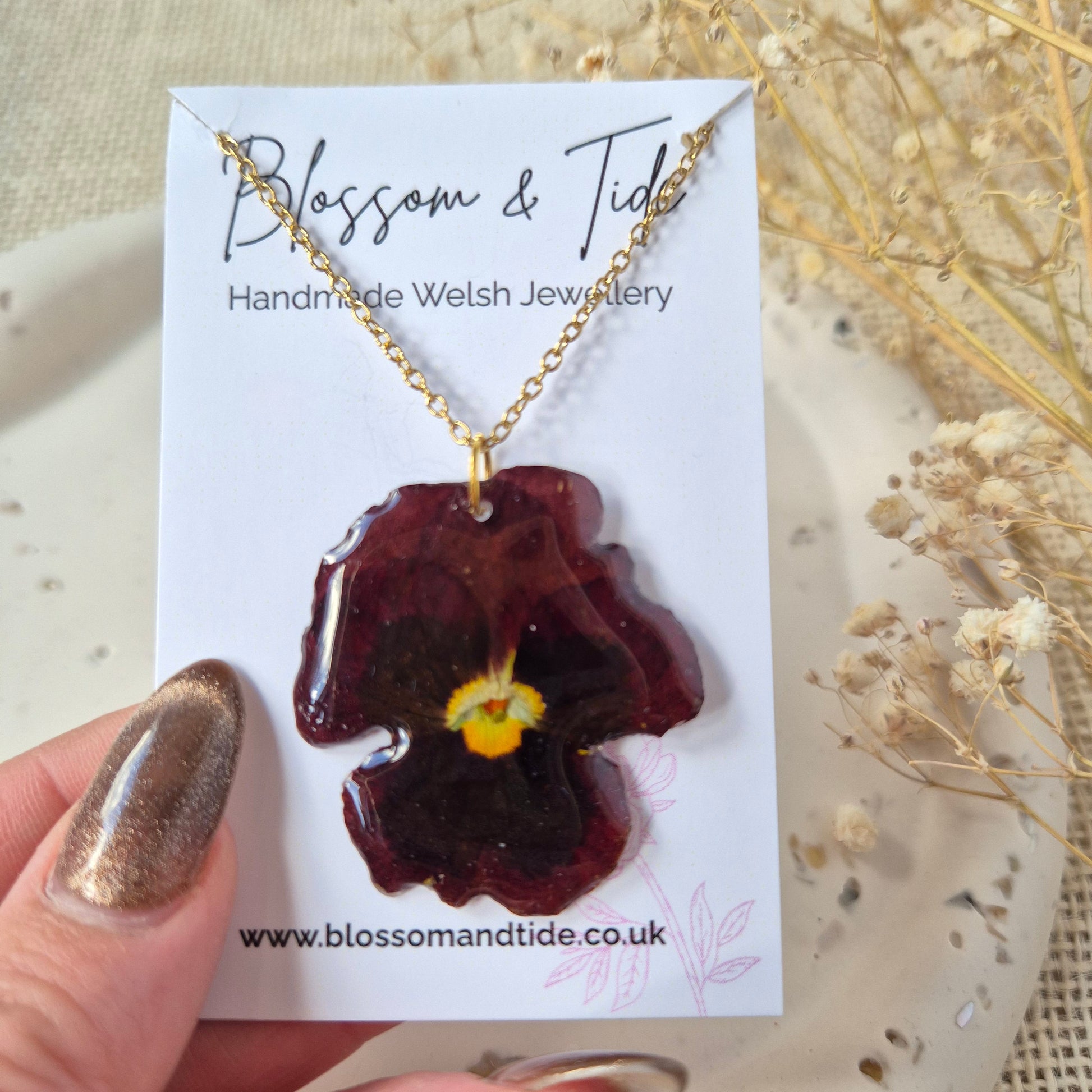 Handmade necklace with a flower pendant on a branded card, held by a hand.