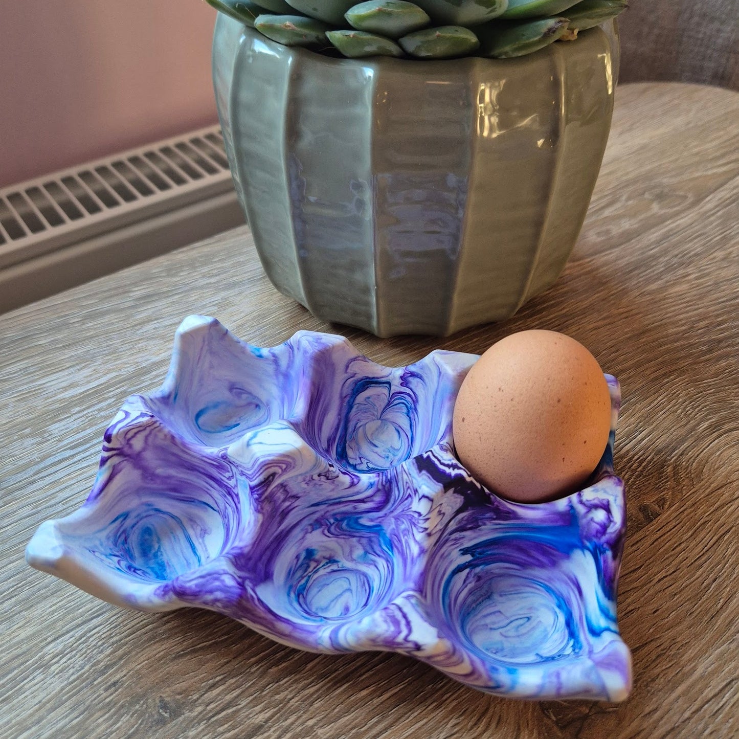 Purple and blue marble egg tray on a wood table with a plant in the background