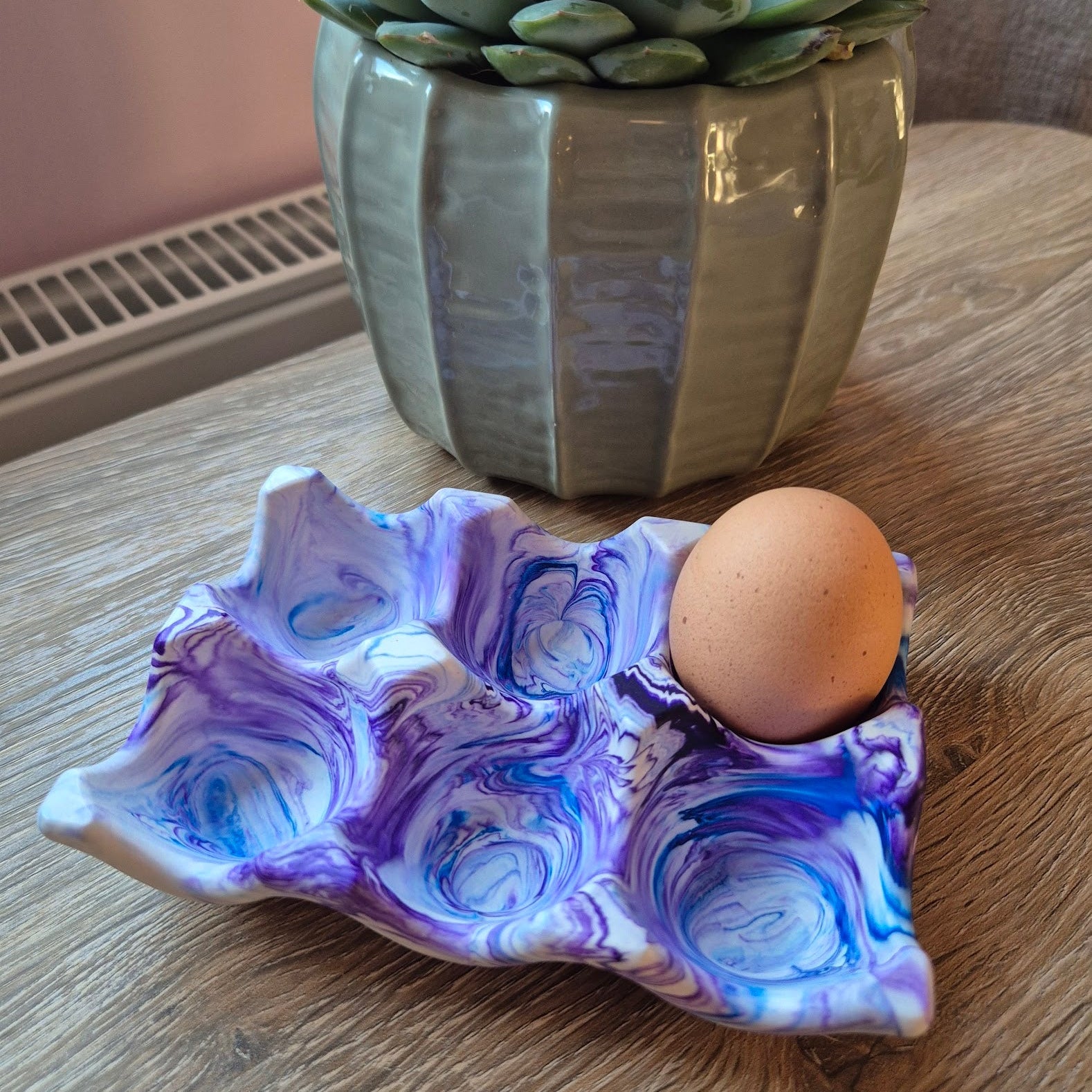 Purple and blue marble egg tray on a wood table with a plant in the background