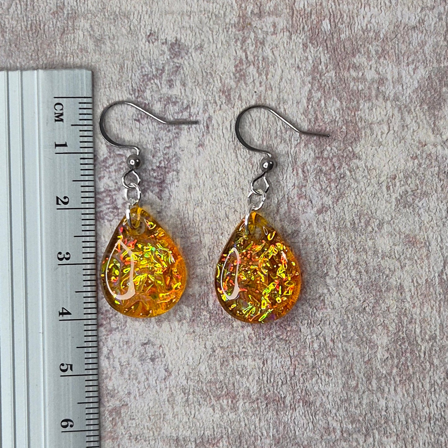 Orange dichroic resin teardrop earrings on a pink background with a ruler for scale