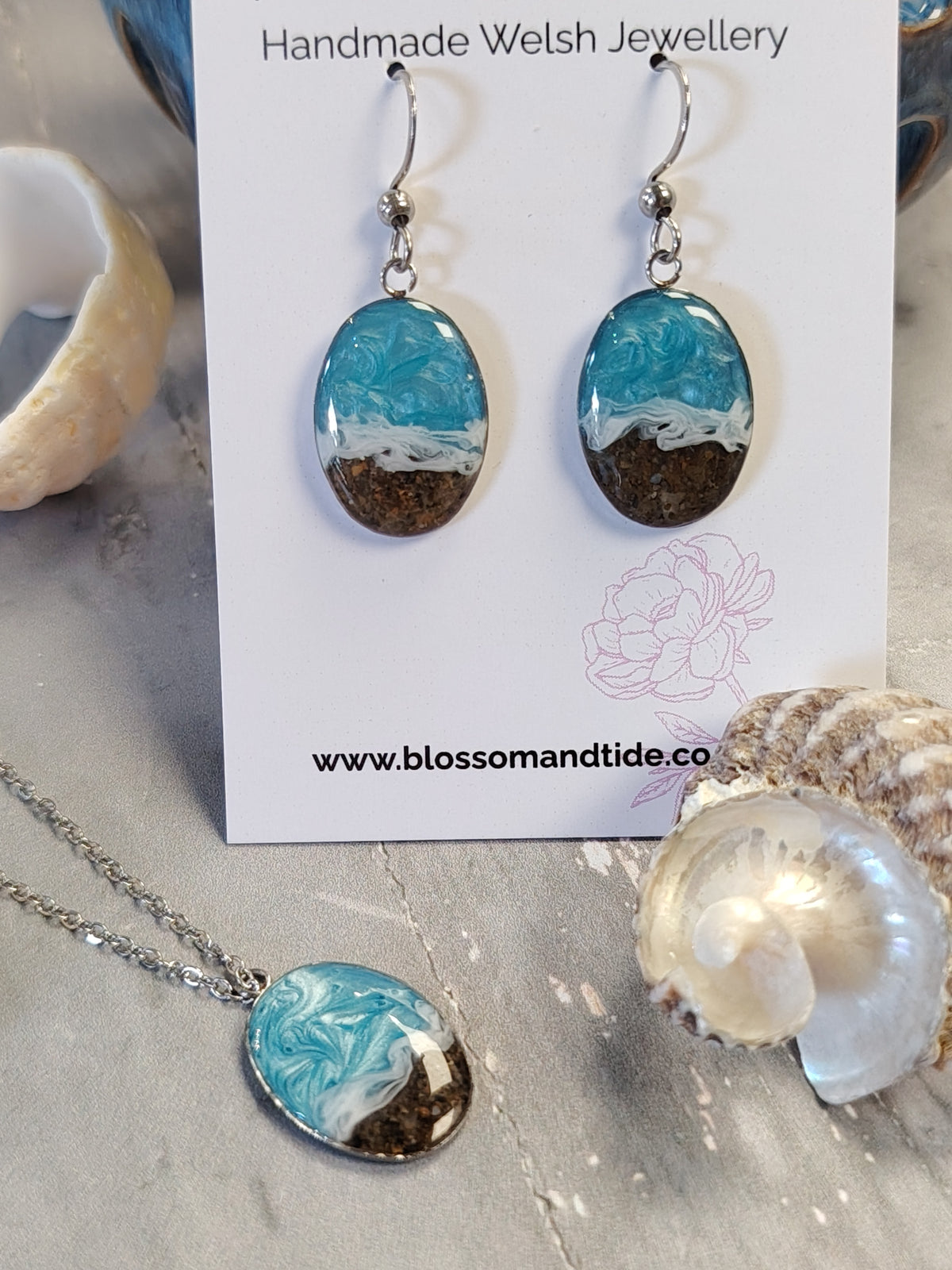 Handmade oval drop earrings and matching necklace with turquoise, white, and brown marbled resin pendants on silver chains, displayed on a white card labeled 'Handmade Welsh Jewellery' with seashells around it.