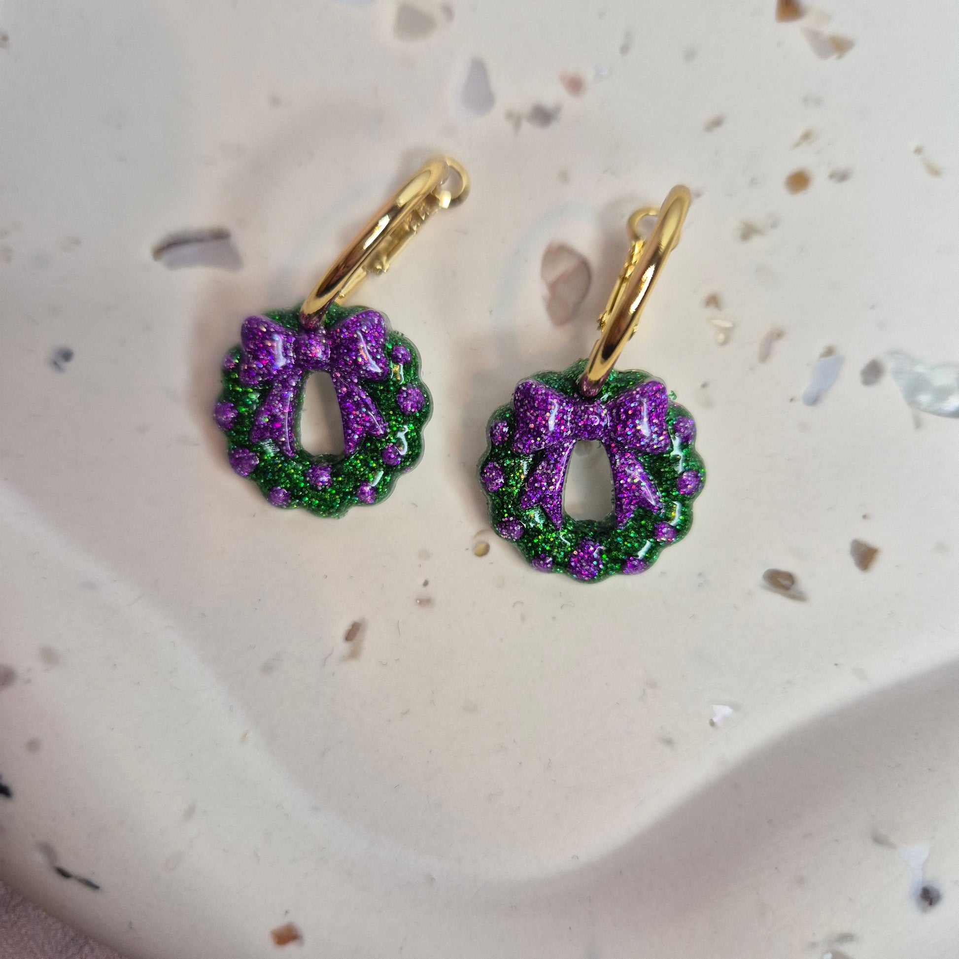 Pair of earrings with green and purple wreath design on a textured surface