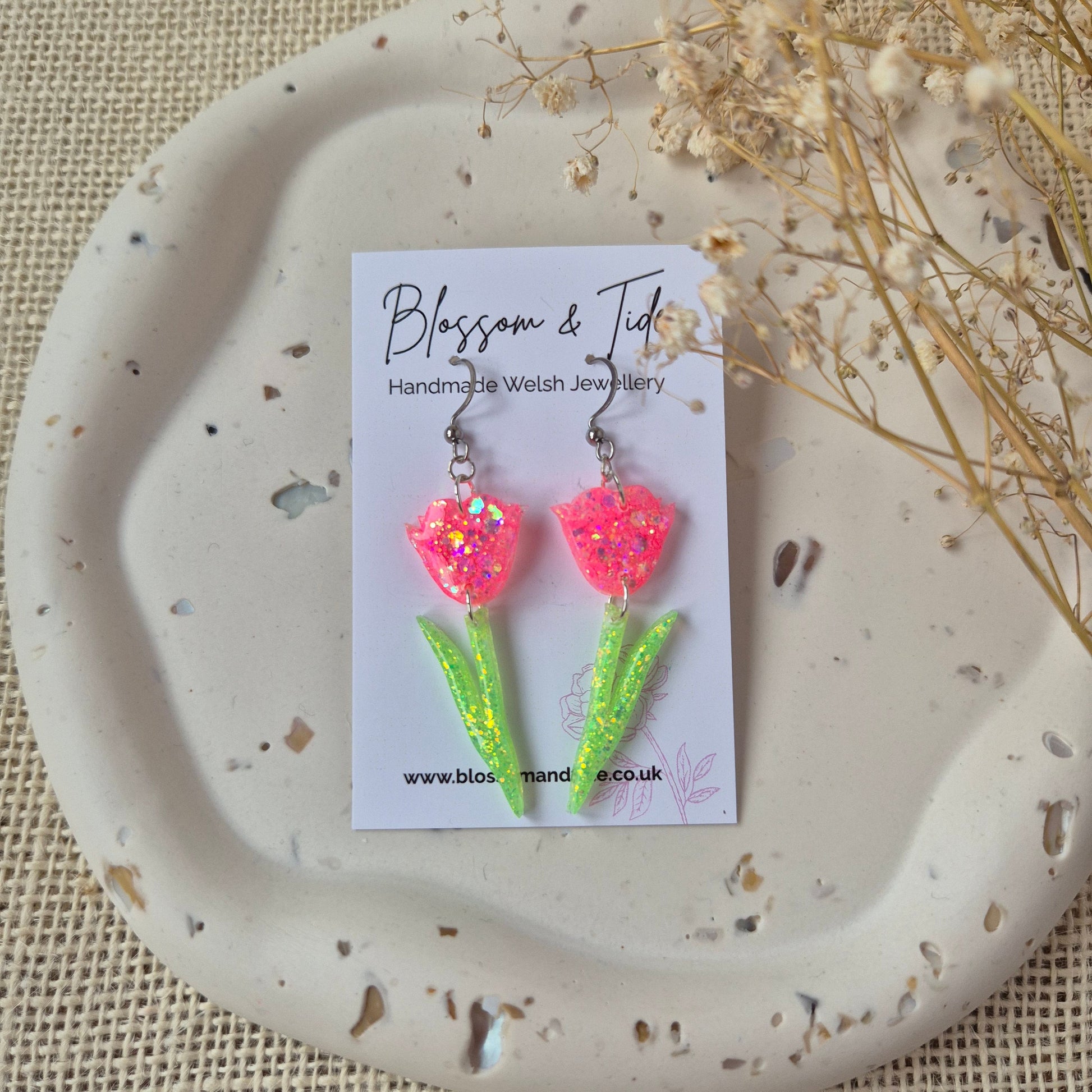 Peach pink glitter tulip dangle earrings with green stems on silver hooks. On branded Blossom & Tide card