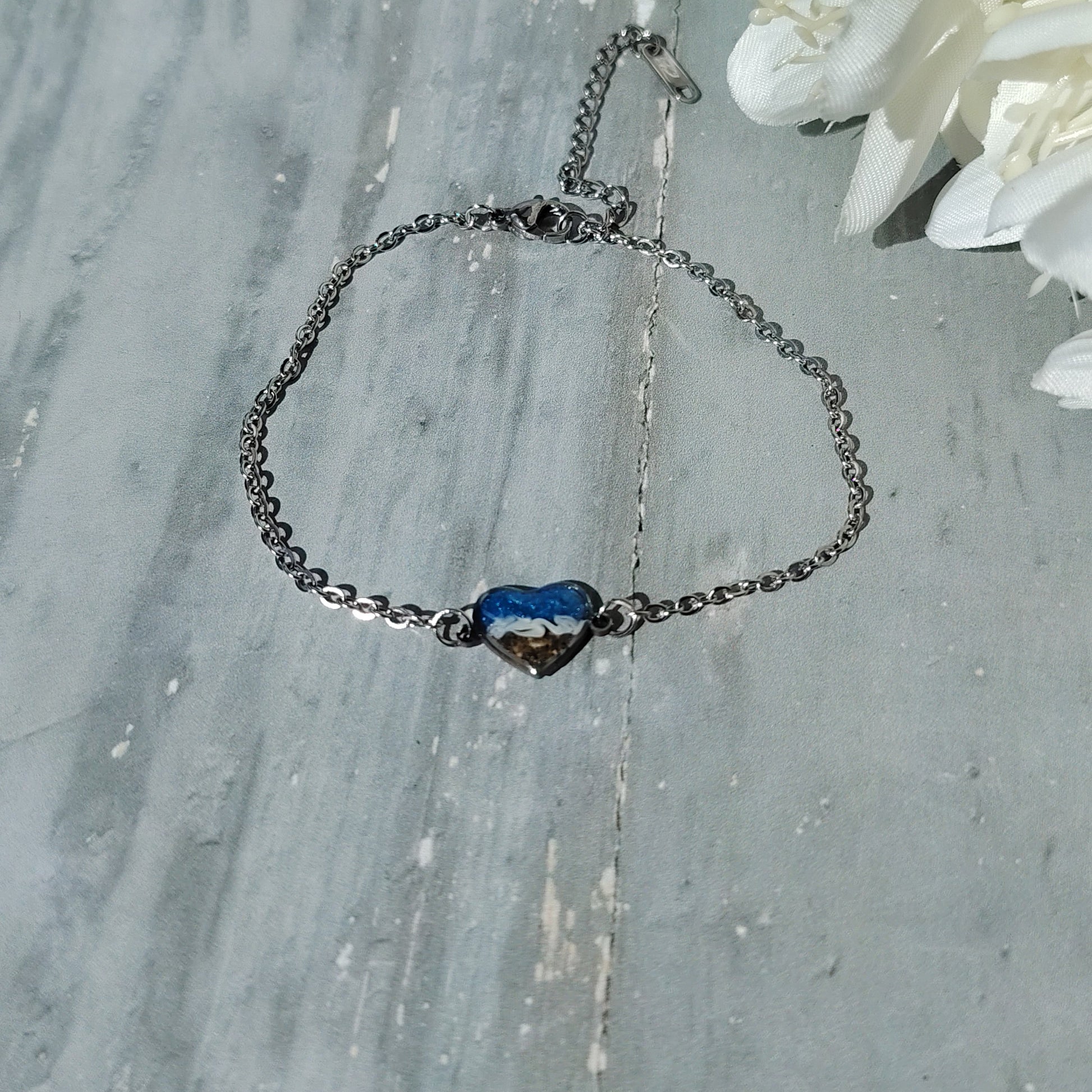 Bracelet with a blue heart charm on a wooden surface with white flowers.