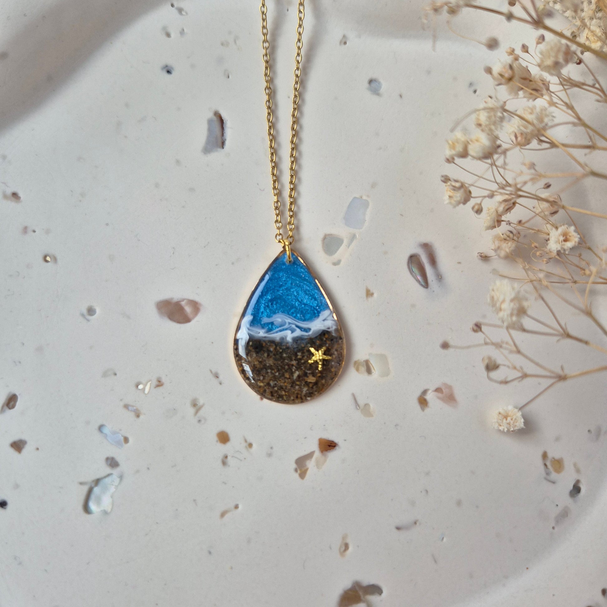 Close up of teardrop pendant necklace made with real Welsh sand and ocean blue resin.