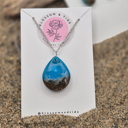  Handmade blue teardrop necklace. Made with real sand from Welsh beaches. Replicating the look of sea and sand. Displayed on a blossom and tide branded card.