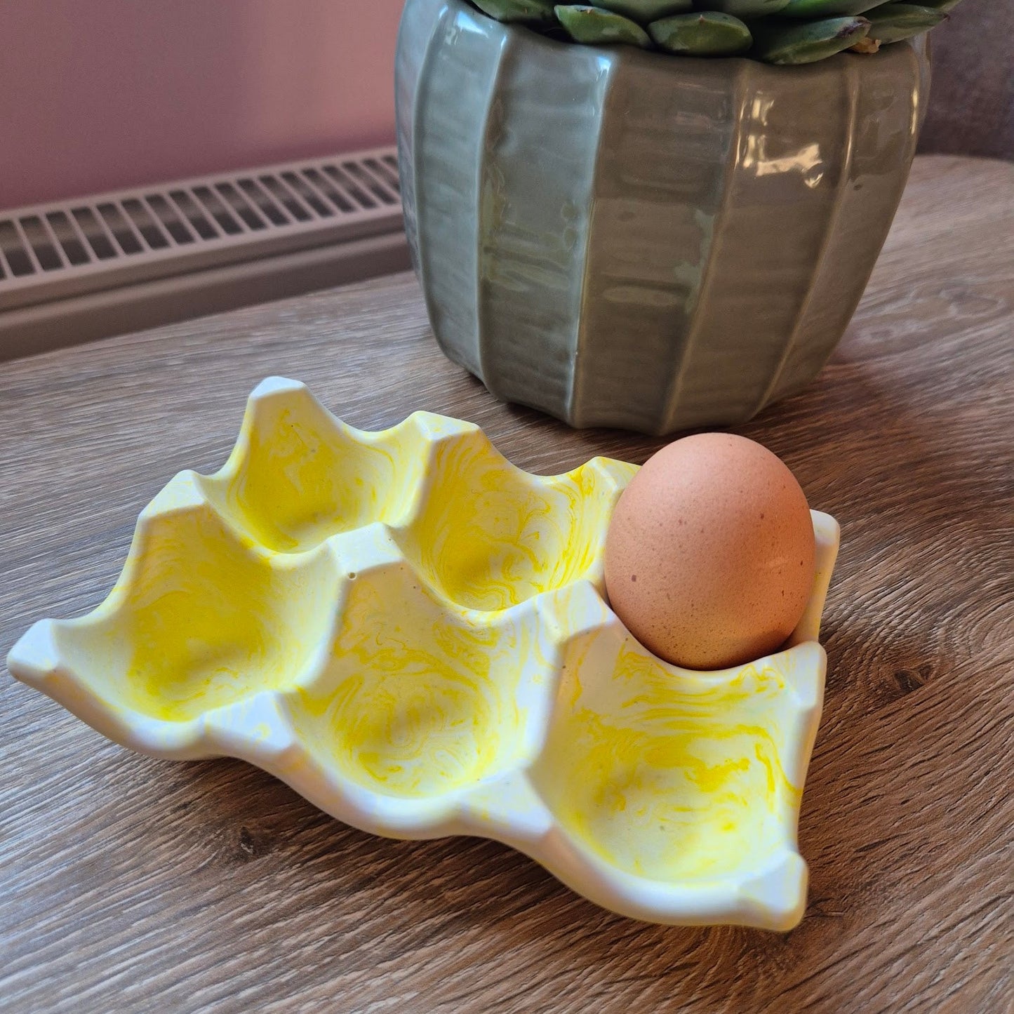 Yellow marble egg tray on a wood table with a plant in the background