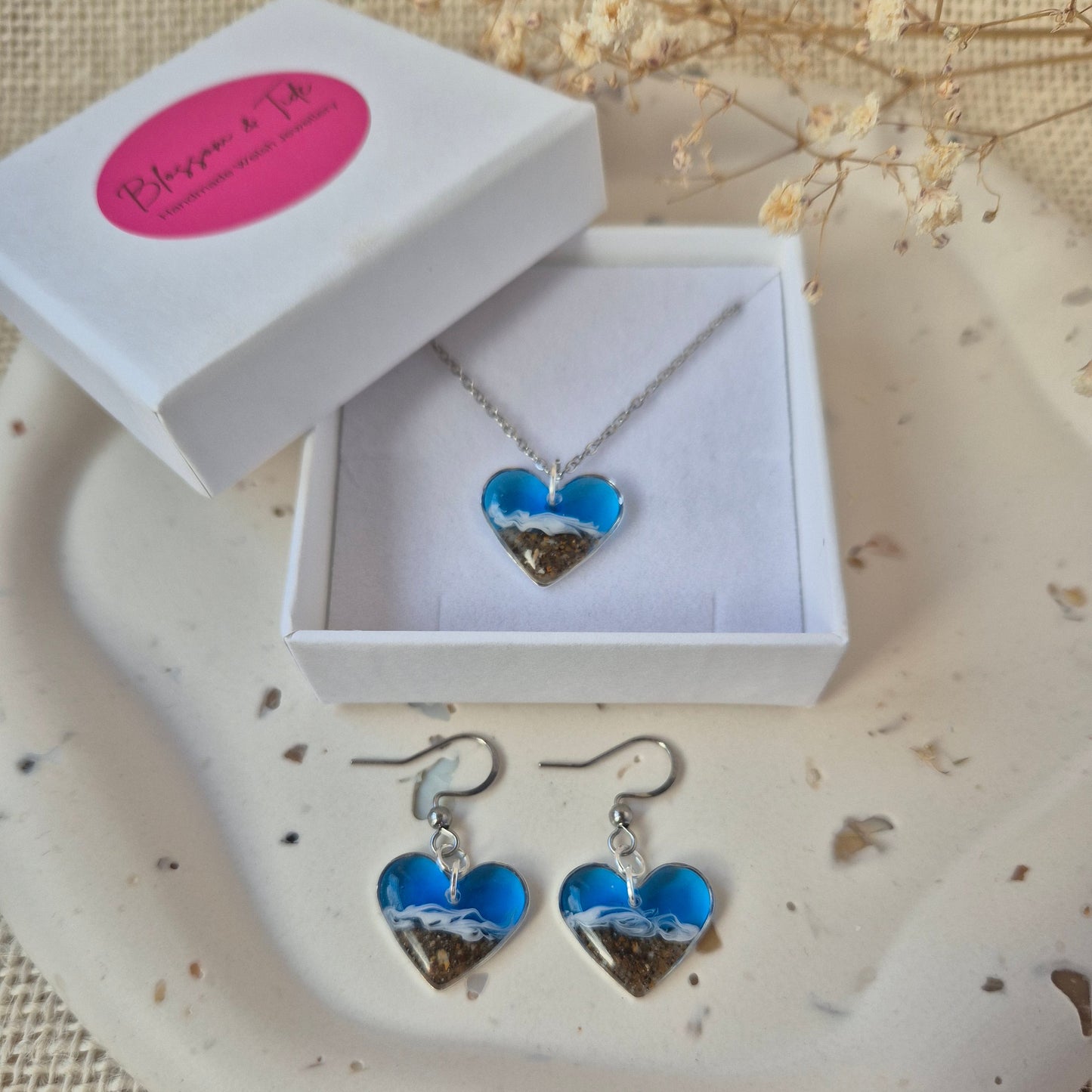 heart beach earrings and necklace in a white box on a textured surface