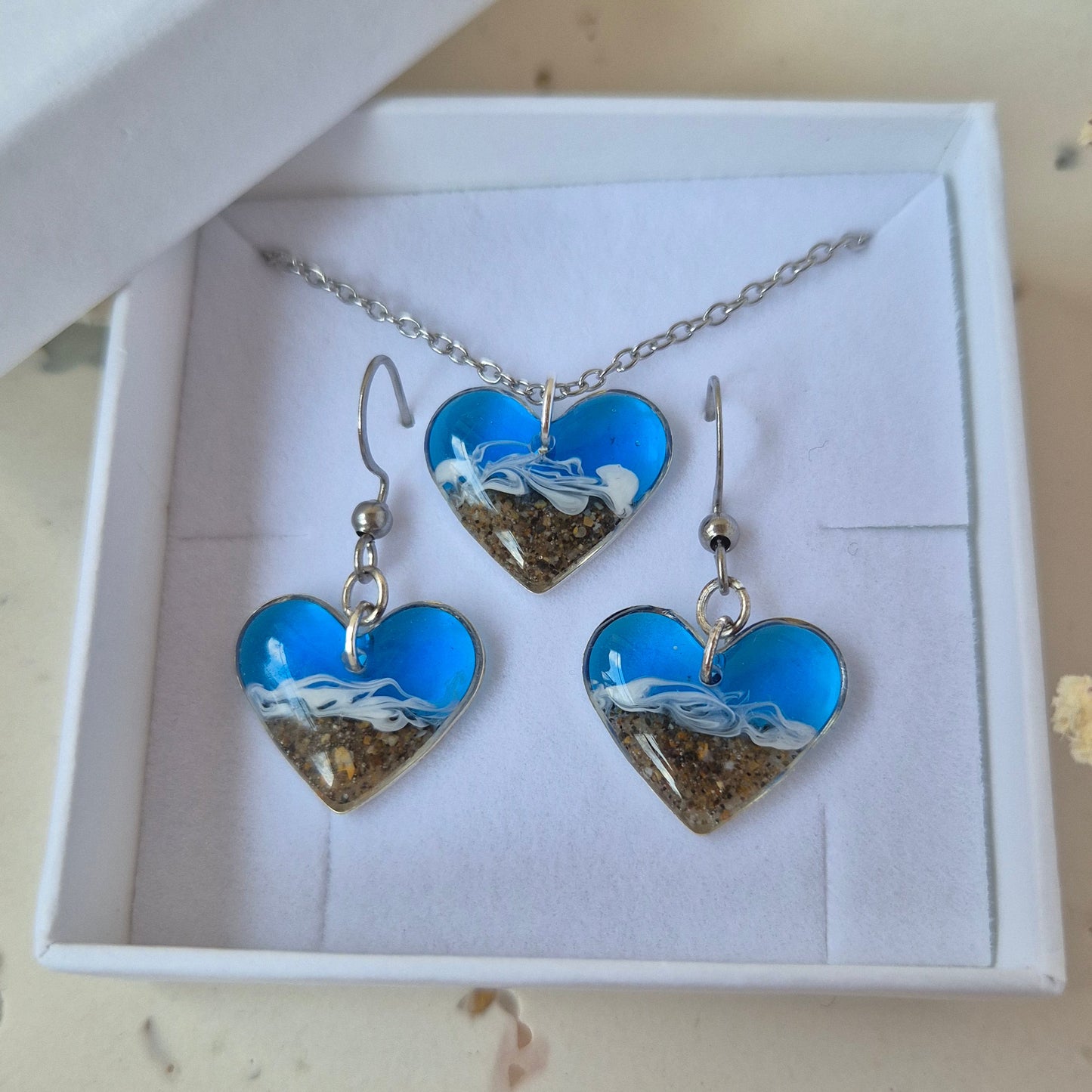 Jewelry set with blue heart-shaped pendant and earrings in a white box on a light  surface.