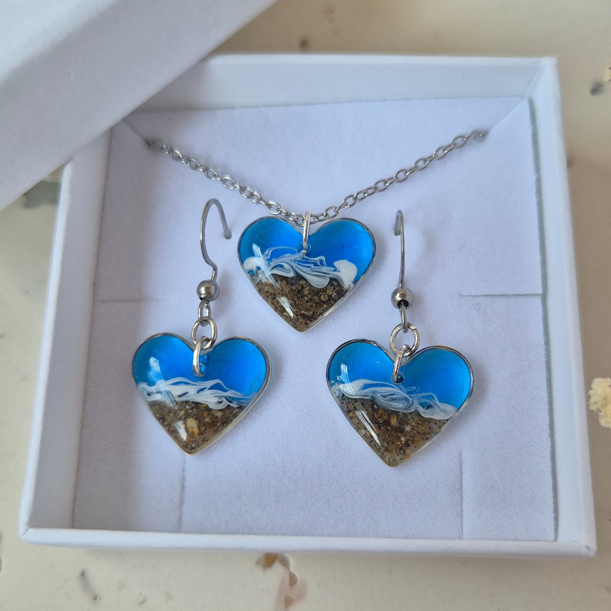 Jewelry set with blue heart-shaped pendant and earrings in a white box on a light  surface.