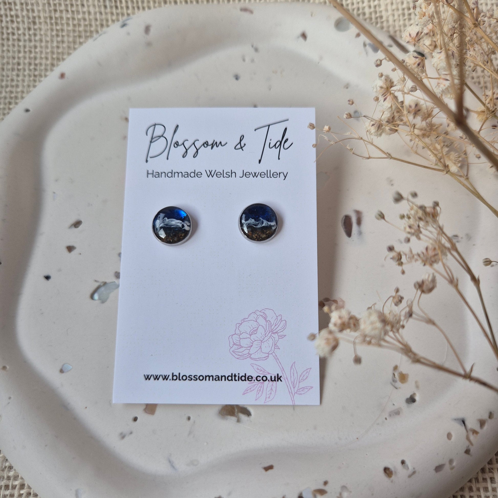 Pair of beach earrings on a branded card with a decorative plate and dried flowers.