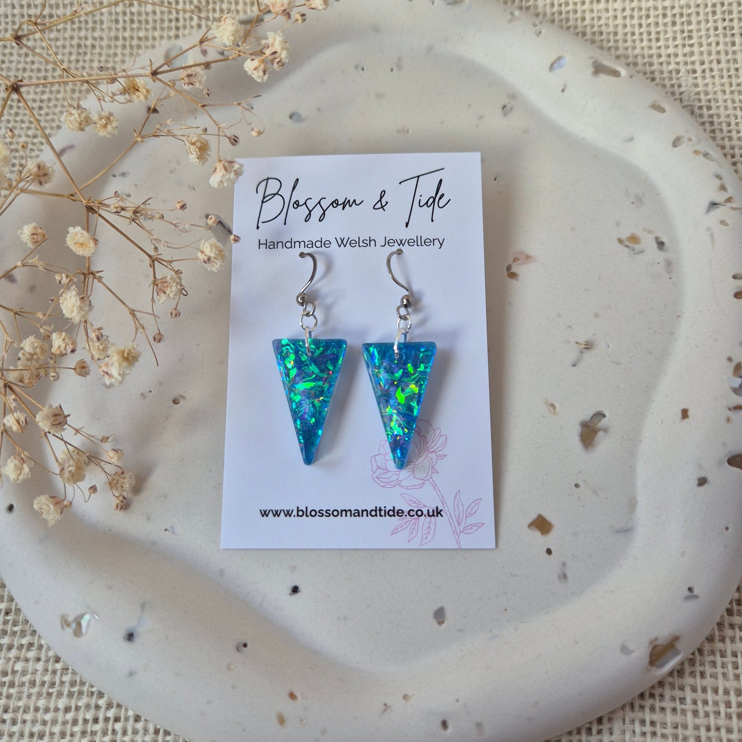 Blue and green  dichroic triangle earrings on a white card with 'Blossom & Tide' branding, displayed on a textured surface.