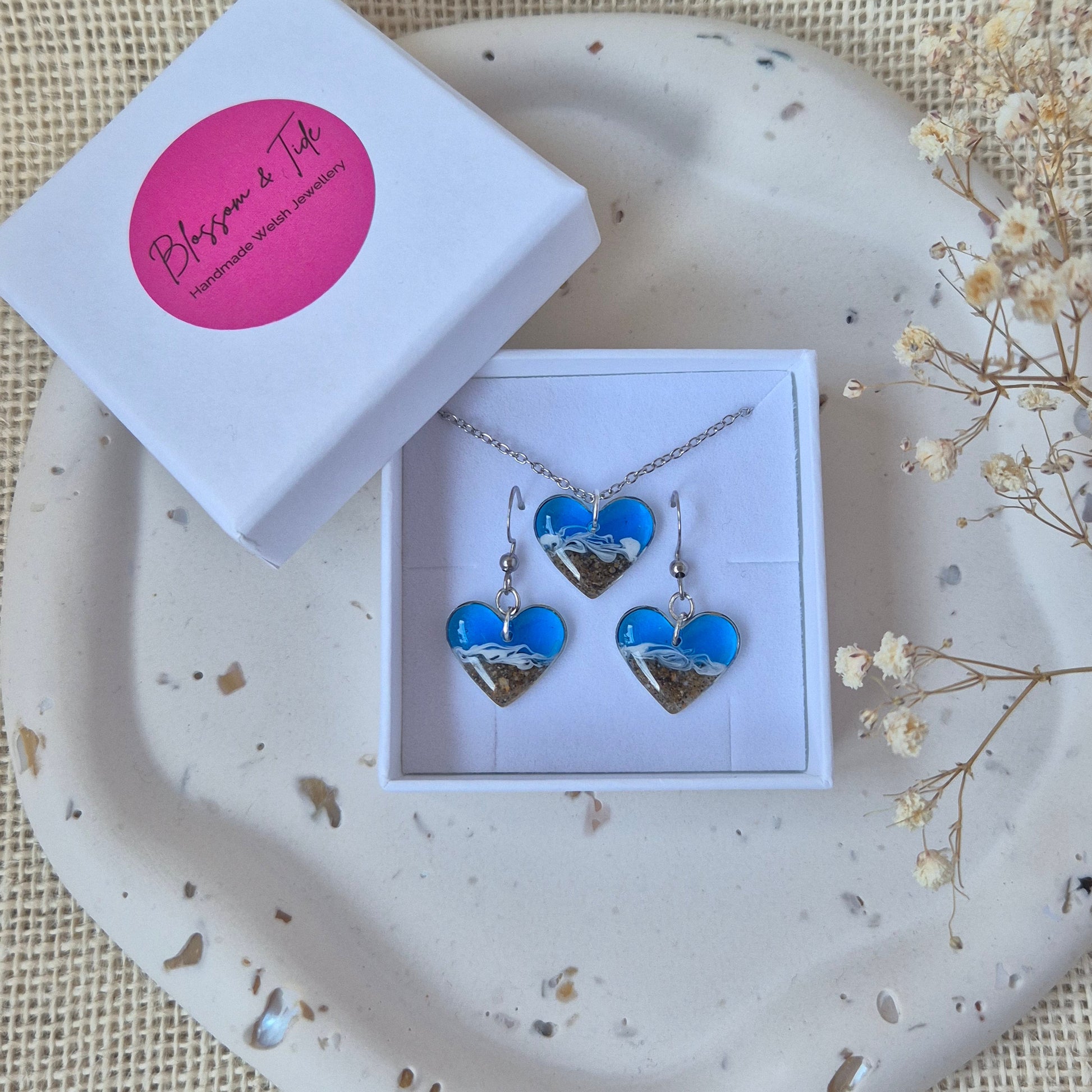 Jewelry set with blue heart sand earrings and necklace in a box on a textured surface