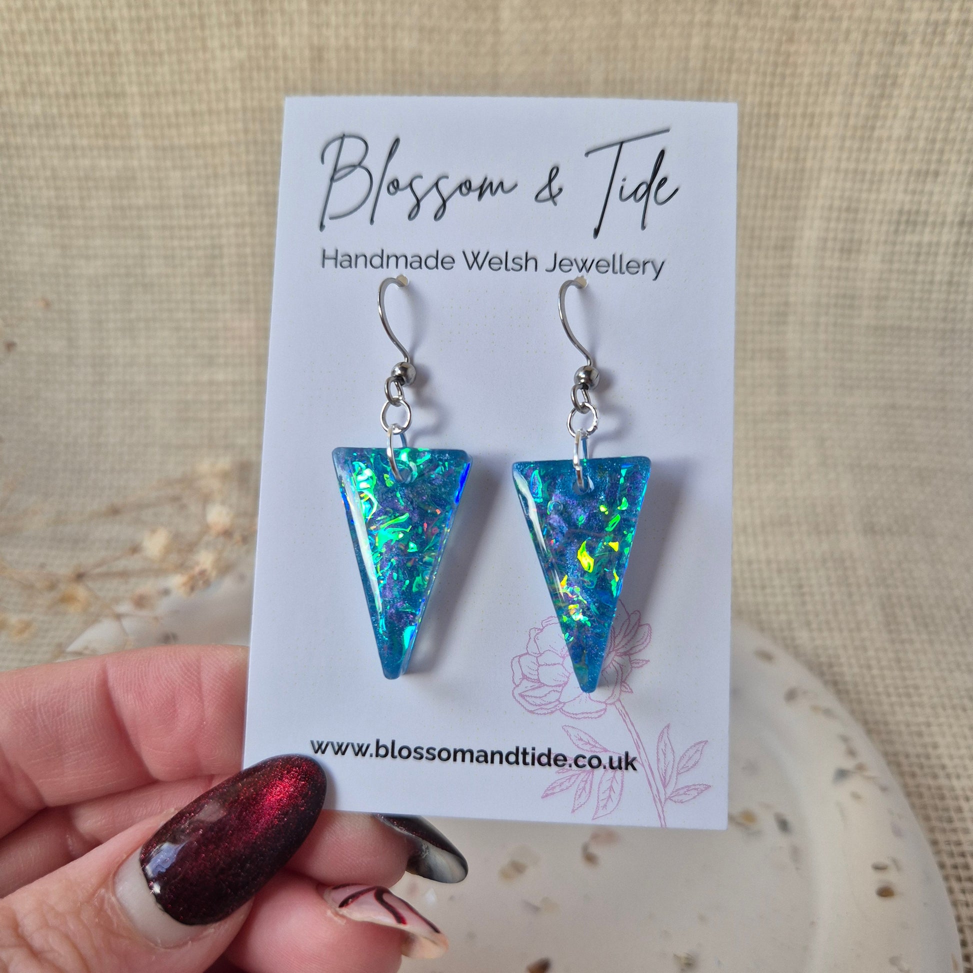 Triangular earrings on a 'Blossom & Tide' branded card held by a hand.