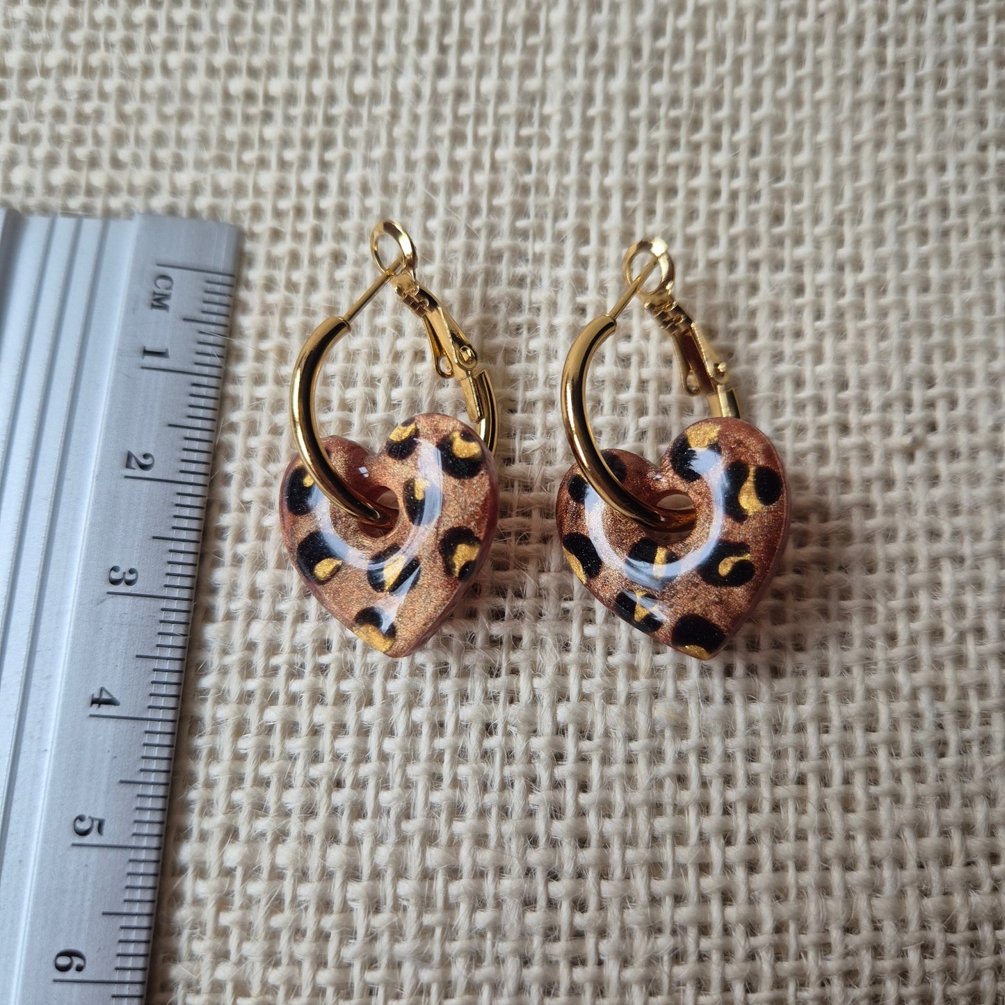 Bronze leopard print earrings next to a ruler for size reference on  a neutral background