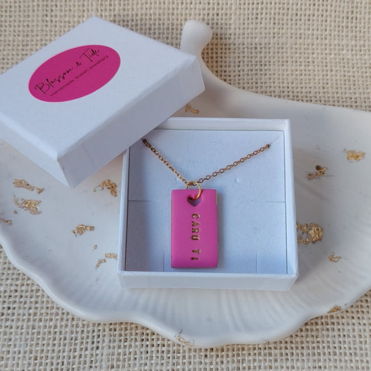 Pink caru ti clay necklace with gold chain in a white box on a textured surface